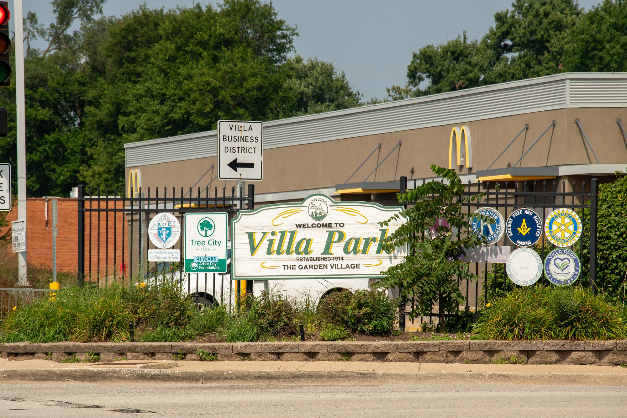 Welcome sign for a village at a street corner near a fast-food restaurant.