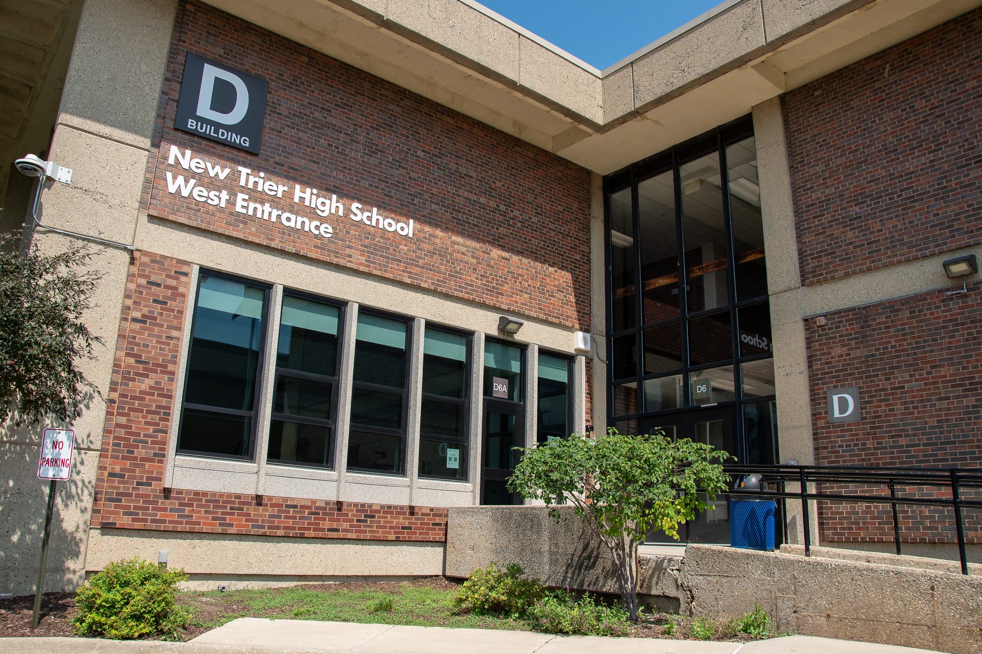 Brick high school building exterior with a west entrance sign and glass doors.