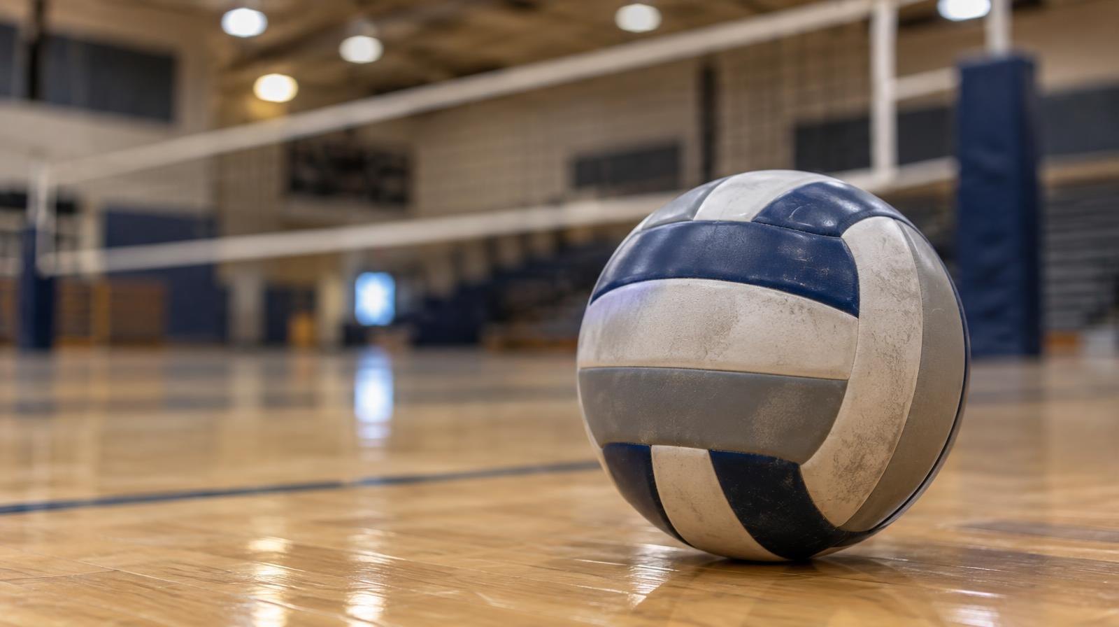 A volleyball sitting on a hardwood gym floor near a net.