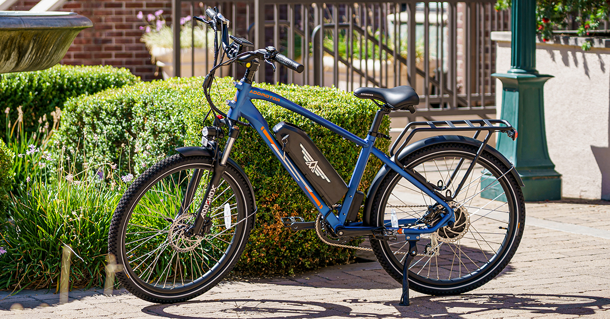 A blue electric bicycle parked on a brick patio near green hedges.