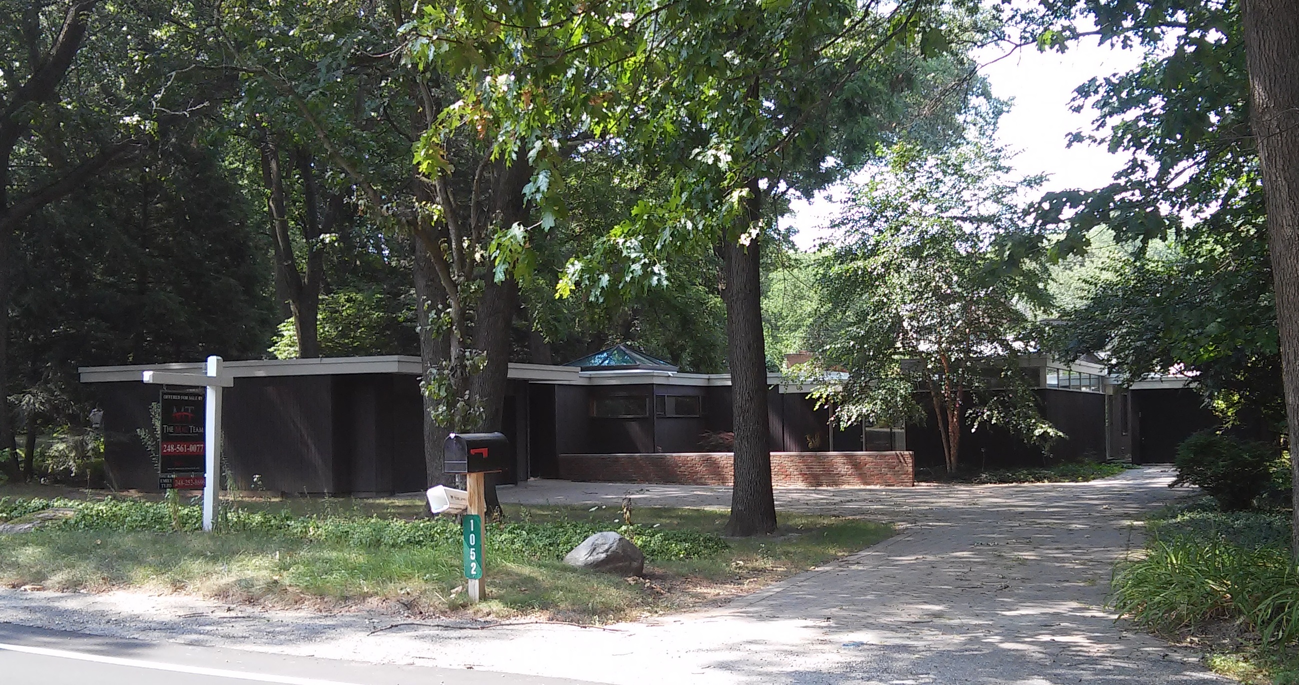 A for-sale sign in the front yard of a single-family home surrounded by trees.