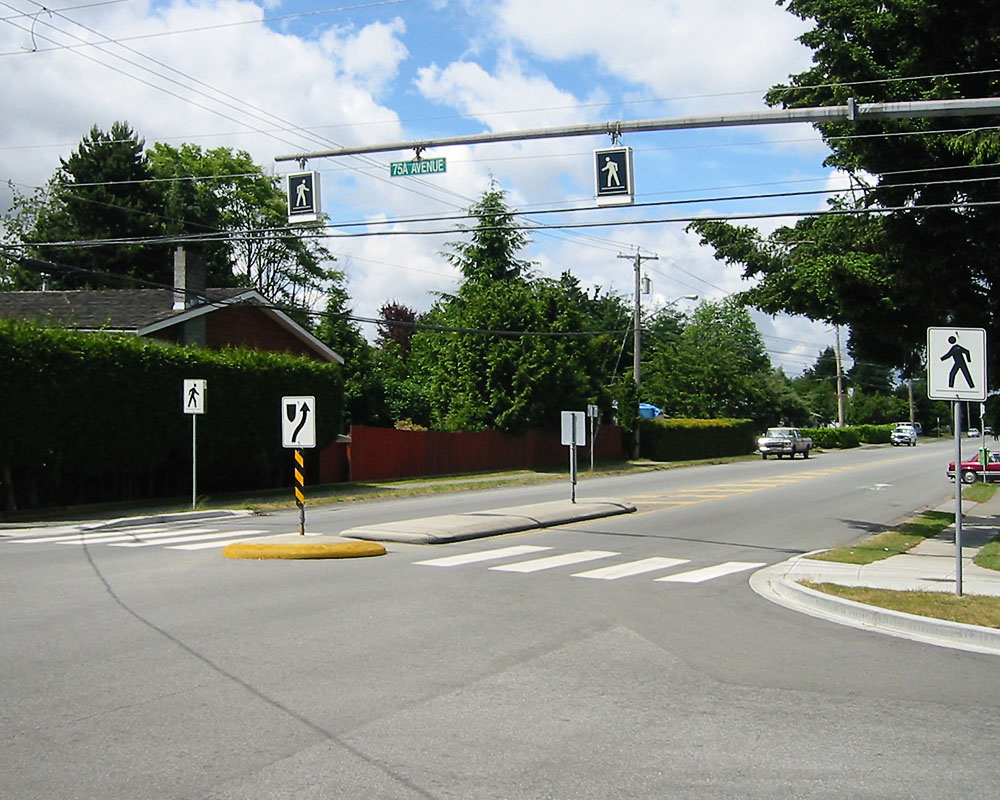 Raised median island and striped crosswalk at a suburban intersection with pedestrian signals.