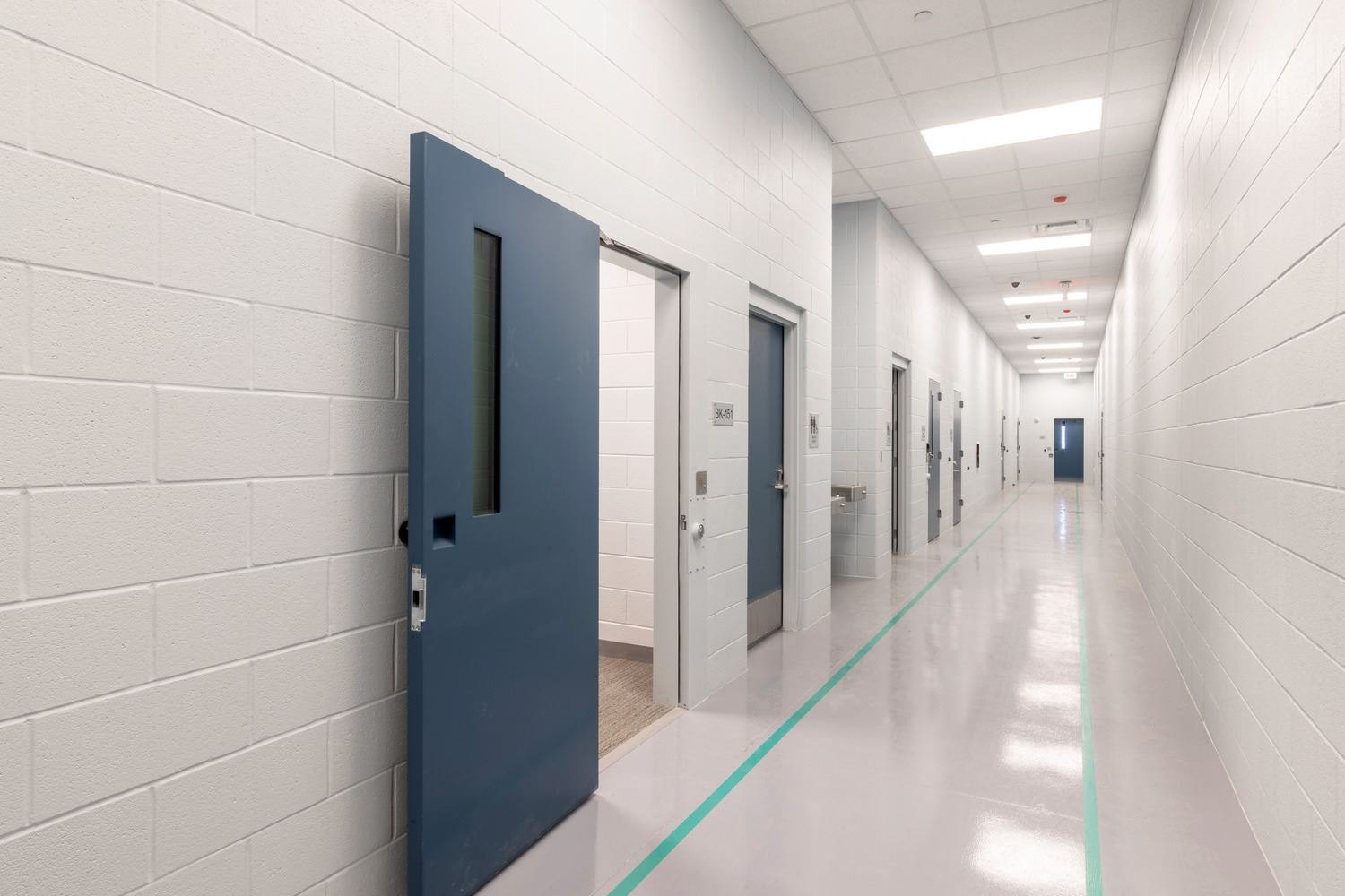 Long institutional hallway with blue steel security doors and polished white floors.