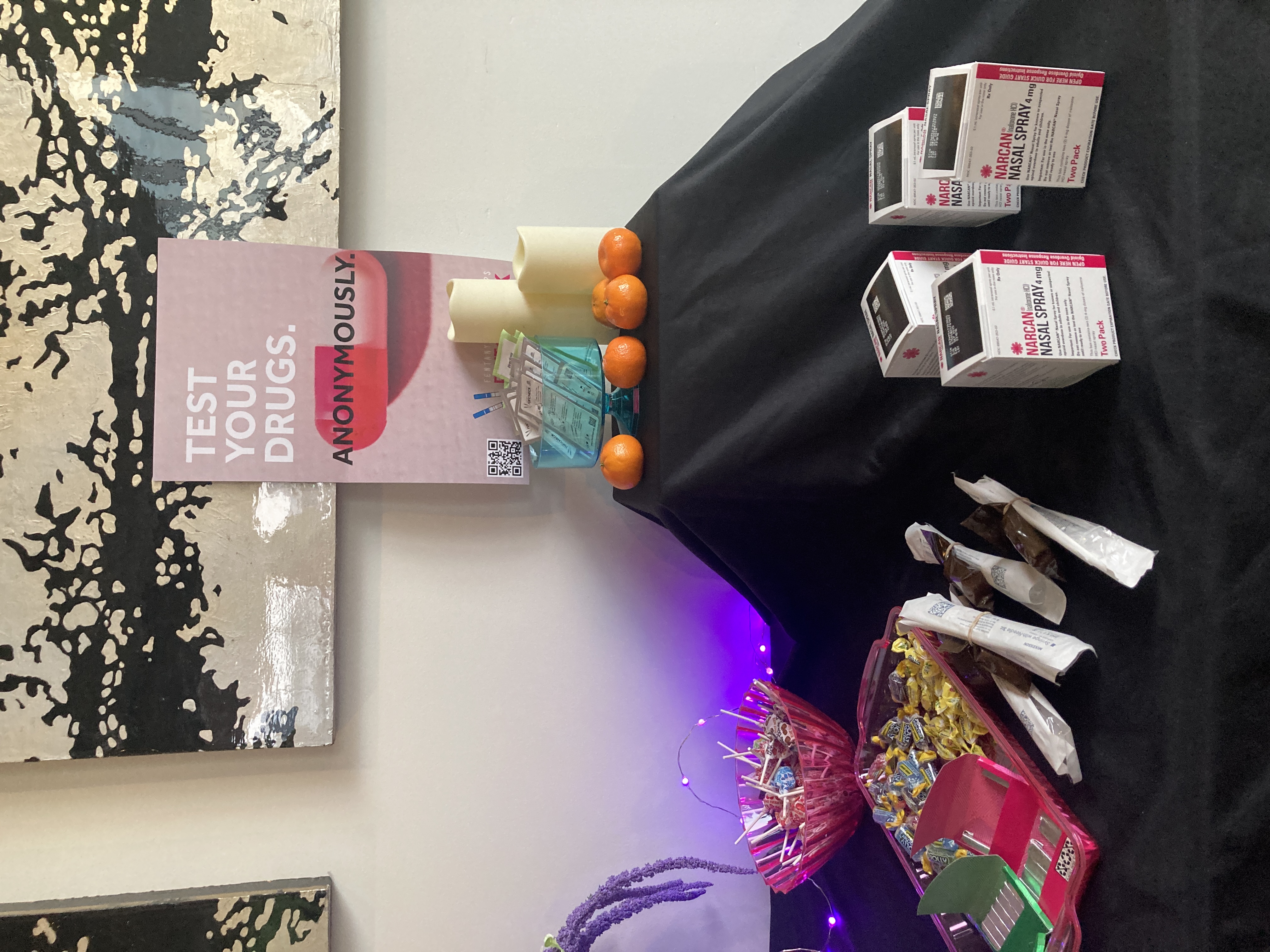 Table covered in Narcan boxes, fentanyl test strips, and a sign reading 'Test Your Drugs. Anonymously.'