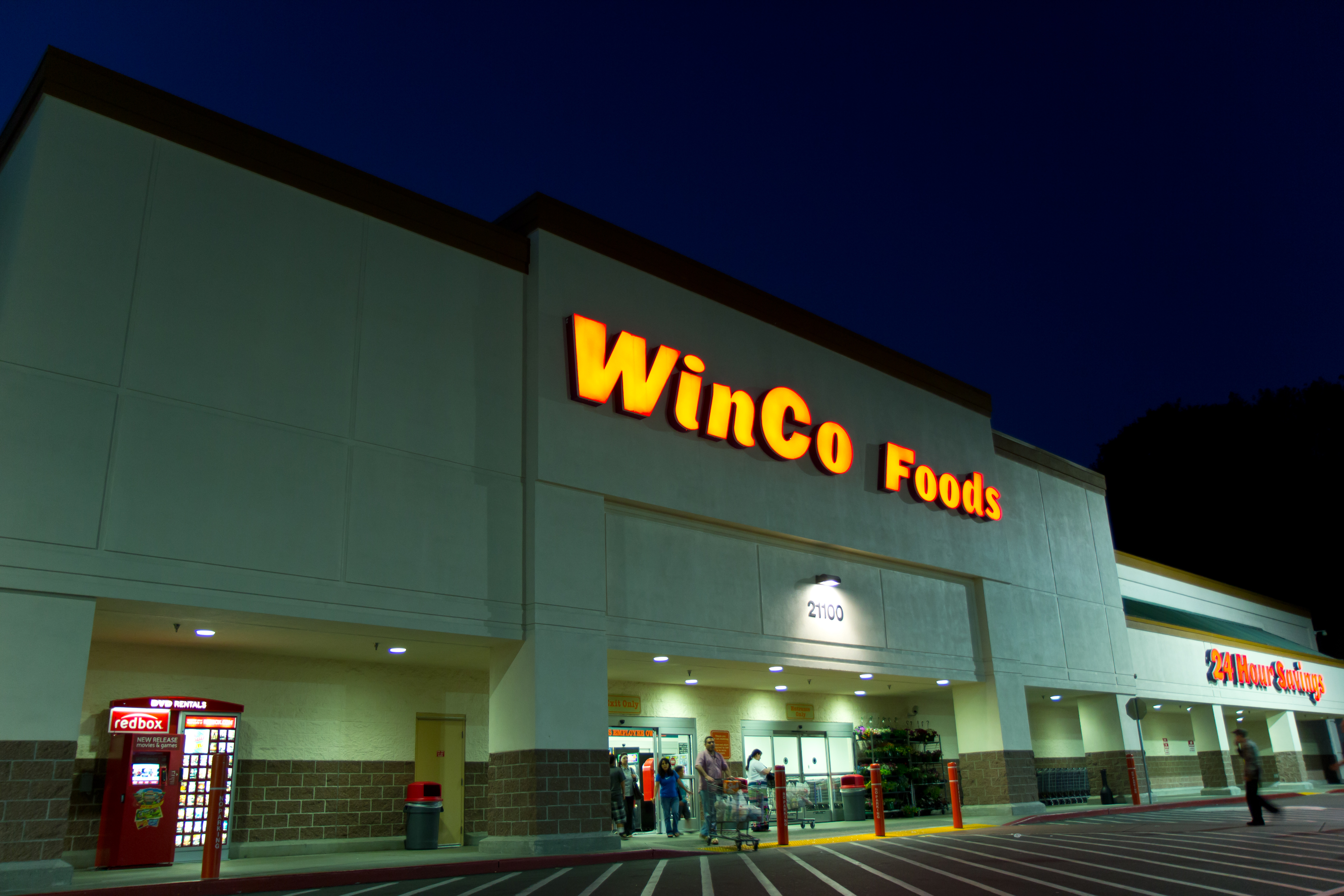 Grocery store exterior at night with illuminated signage and shopping carts near the entrance.