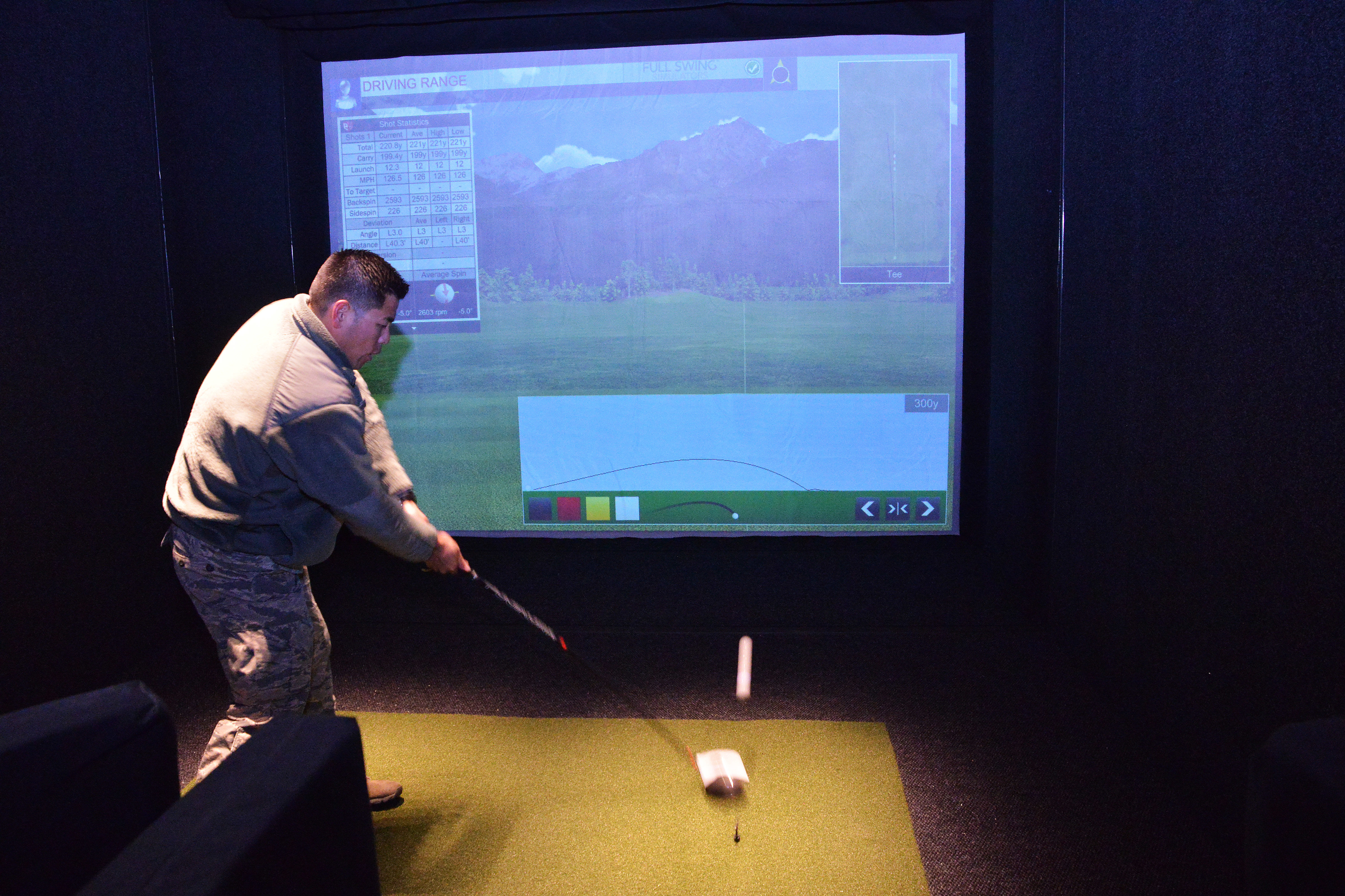 Person swinging a golf club on a turf mat inside an indoor golf simulator.