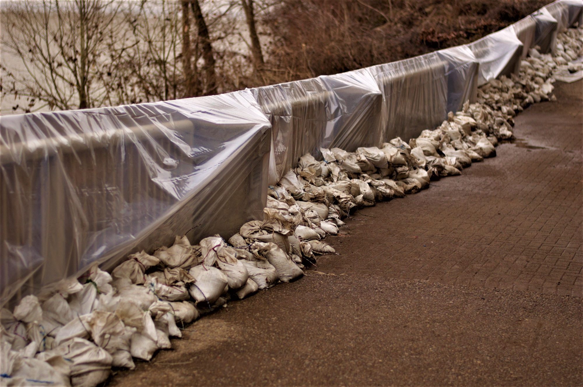 An arrangement of sandbags and plastic sheeting for flood protection along a riverside road.