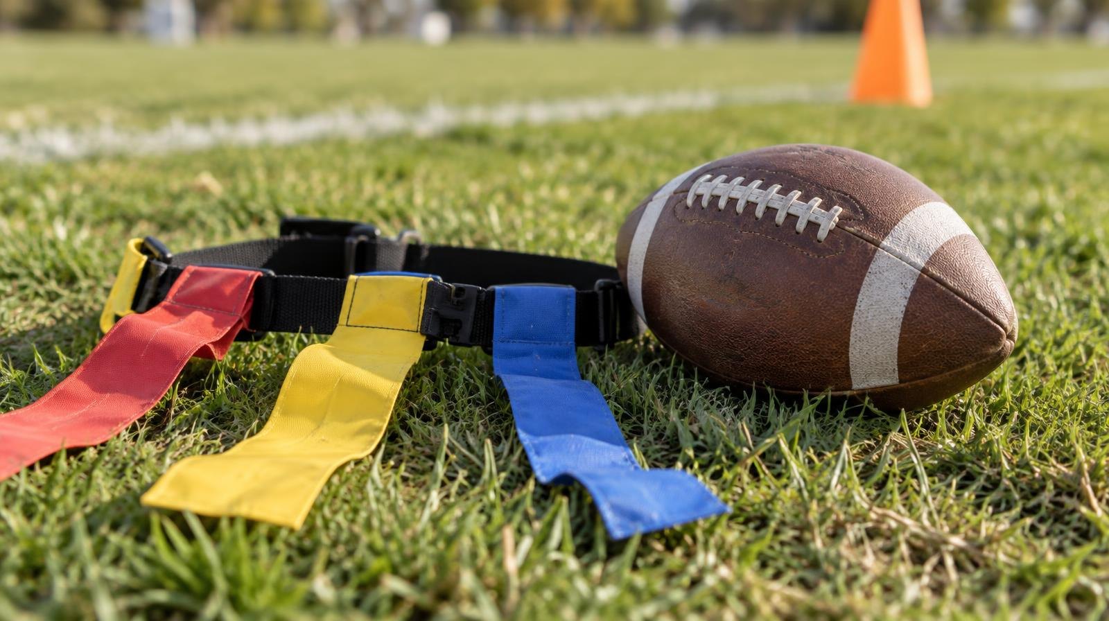 A flag football belt with colorful flags lying on green grass beside a football.