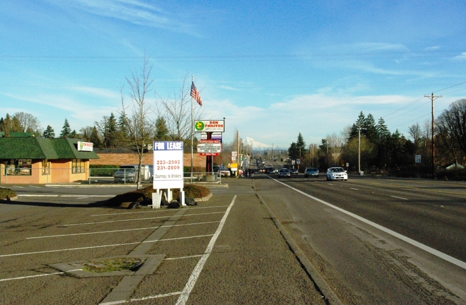 Multi-lane highway lined with commercial signs in Aloha, Oregon, with Mount Hood in the distance.