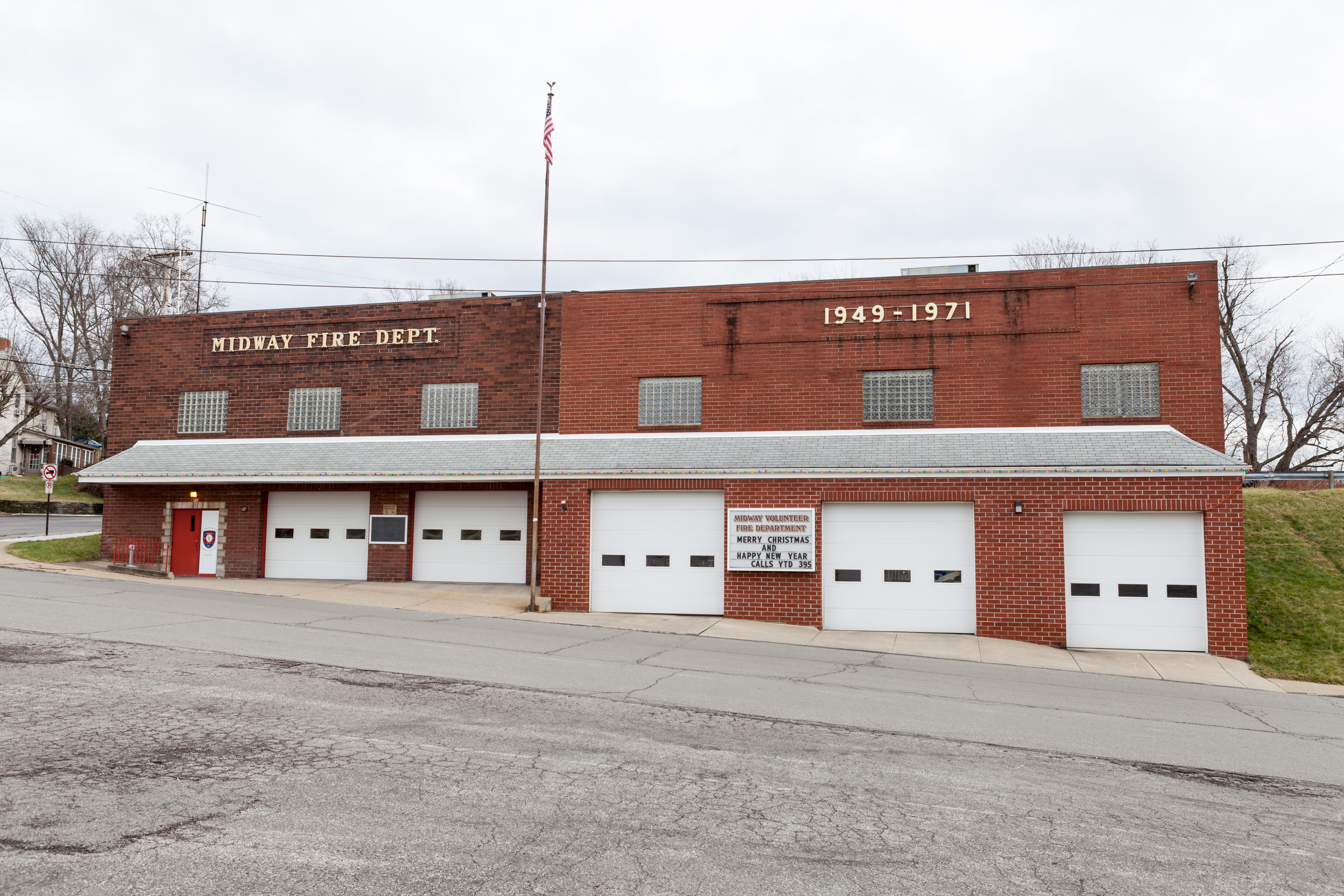 Two-story red brick fire station with white garage bay doors and an American flag.