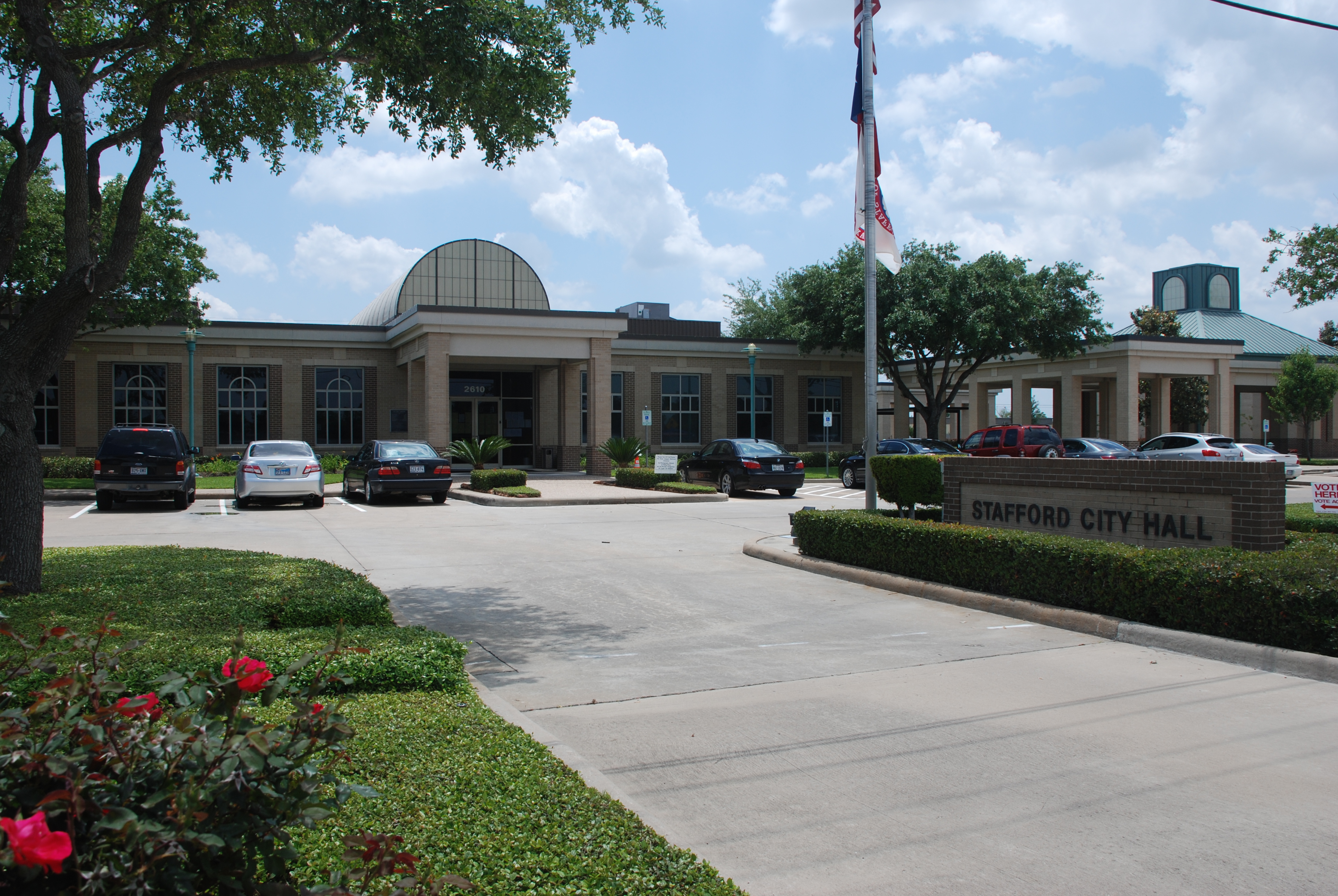 Exterior of Stafford City Hall building with flagpole and parking lot in front.