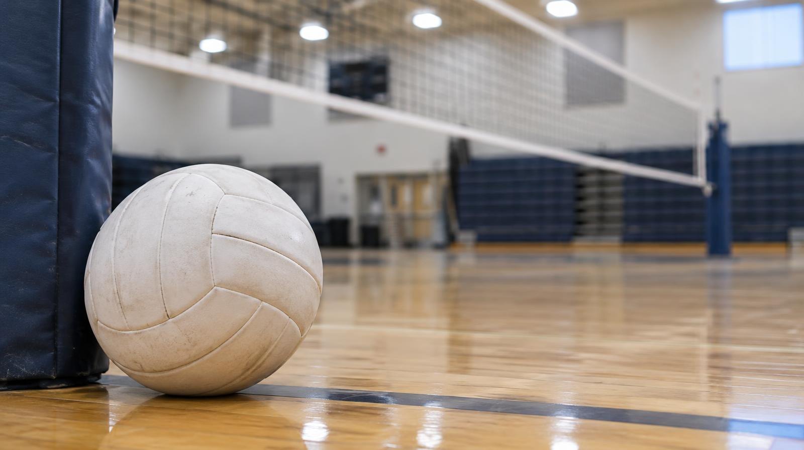 White volleyball on a hardwood gym floor next to a net post.