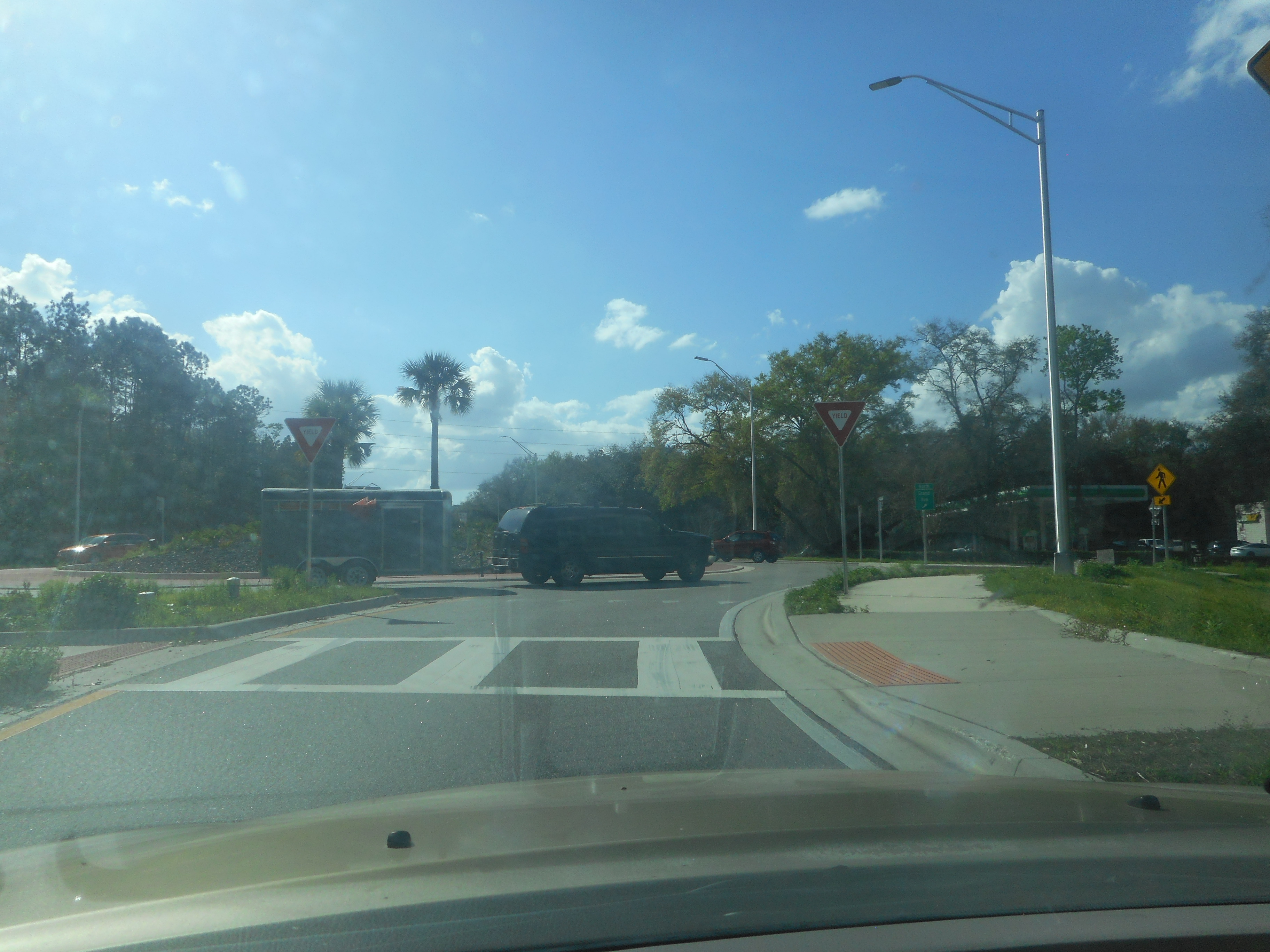 Driver's view of a Florida roundabout with yield signs, a street lamp, and palm trees.