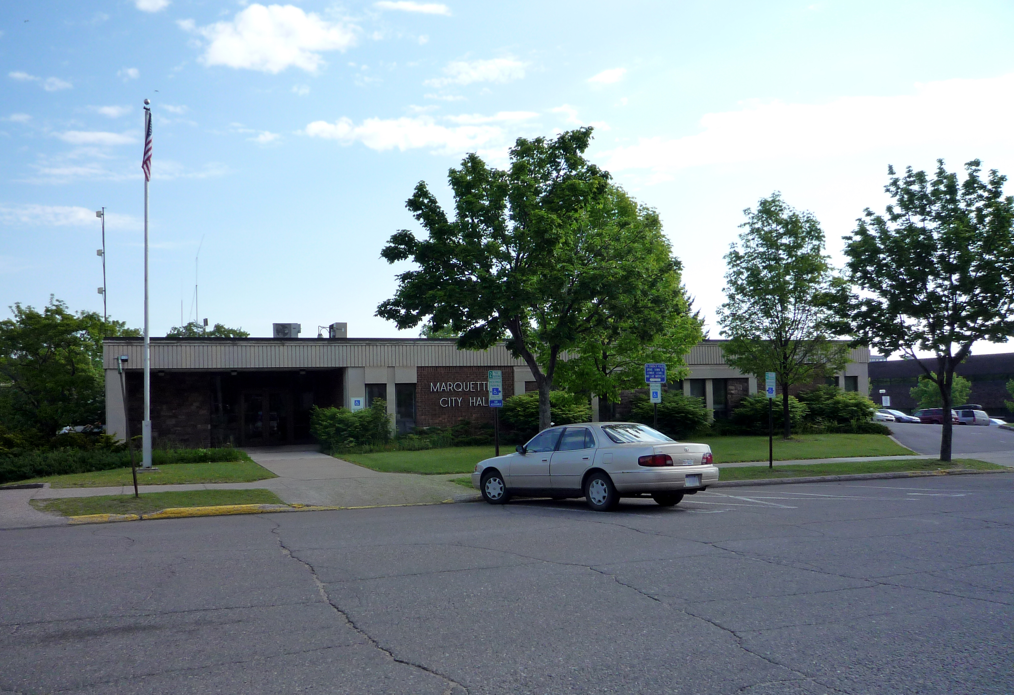 Low-rise municipal building with a Marquette City Hall sign and American flag out front.