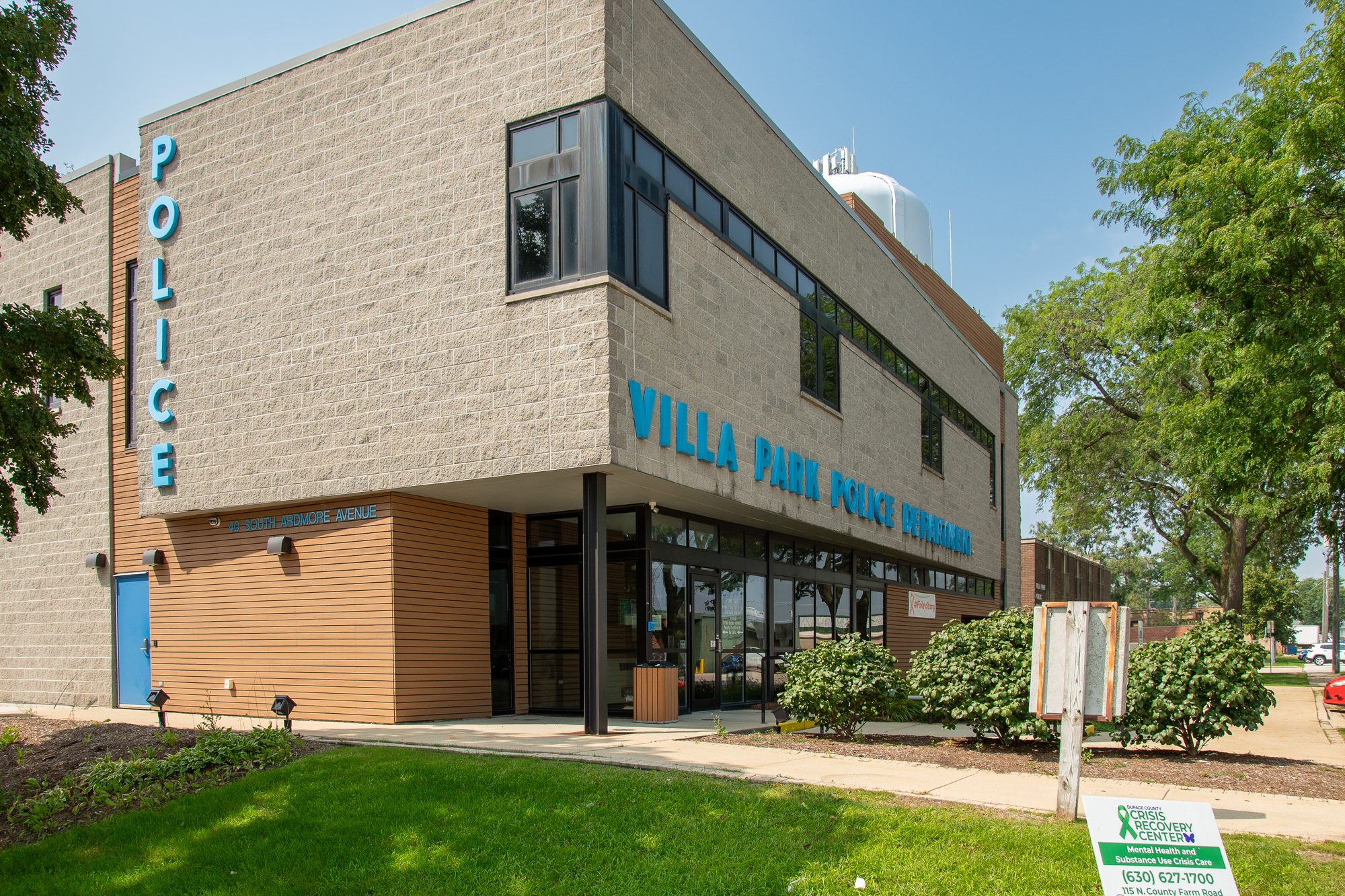 Two-story brick police department building with blue vertical signage on a sunny day.