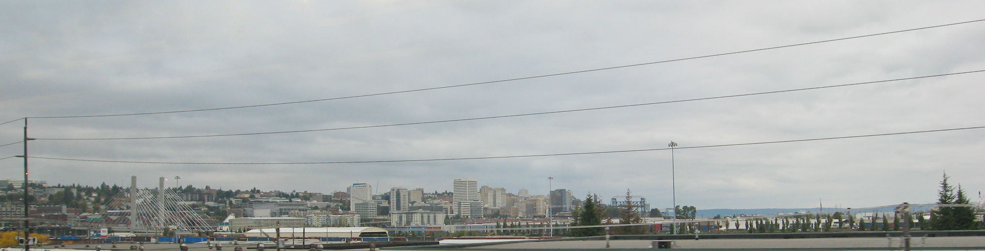 Panoramic cityscape of mid-rise buildings under a cloudy sky with water visible in the background.