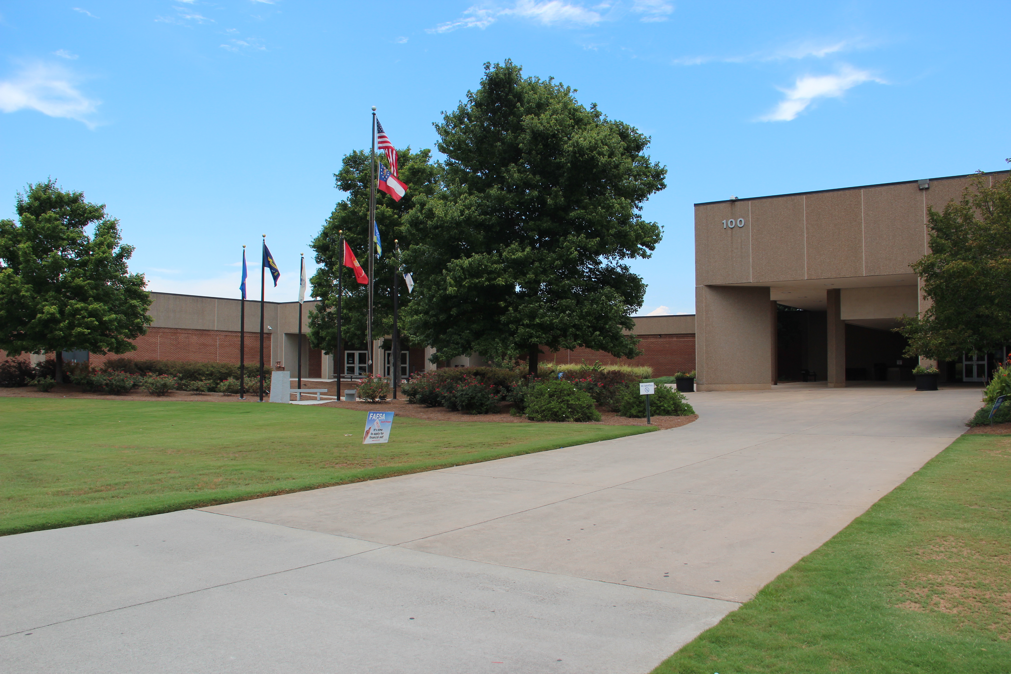Low-rise tan brick college building with flagpoles and a concrete walkway leading to the entrance.