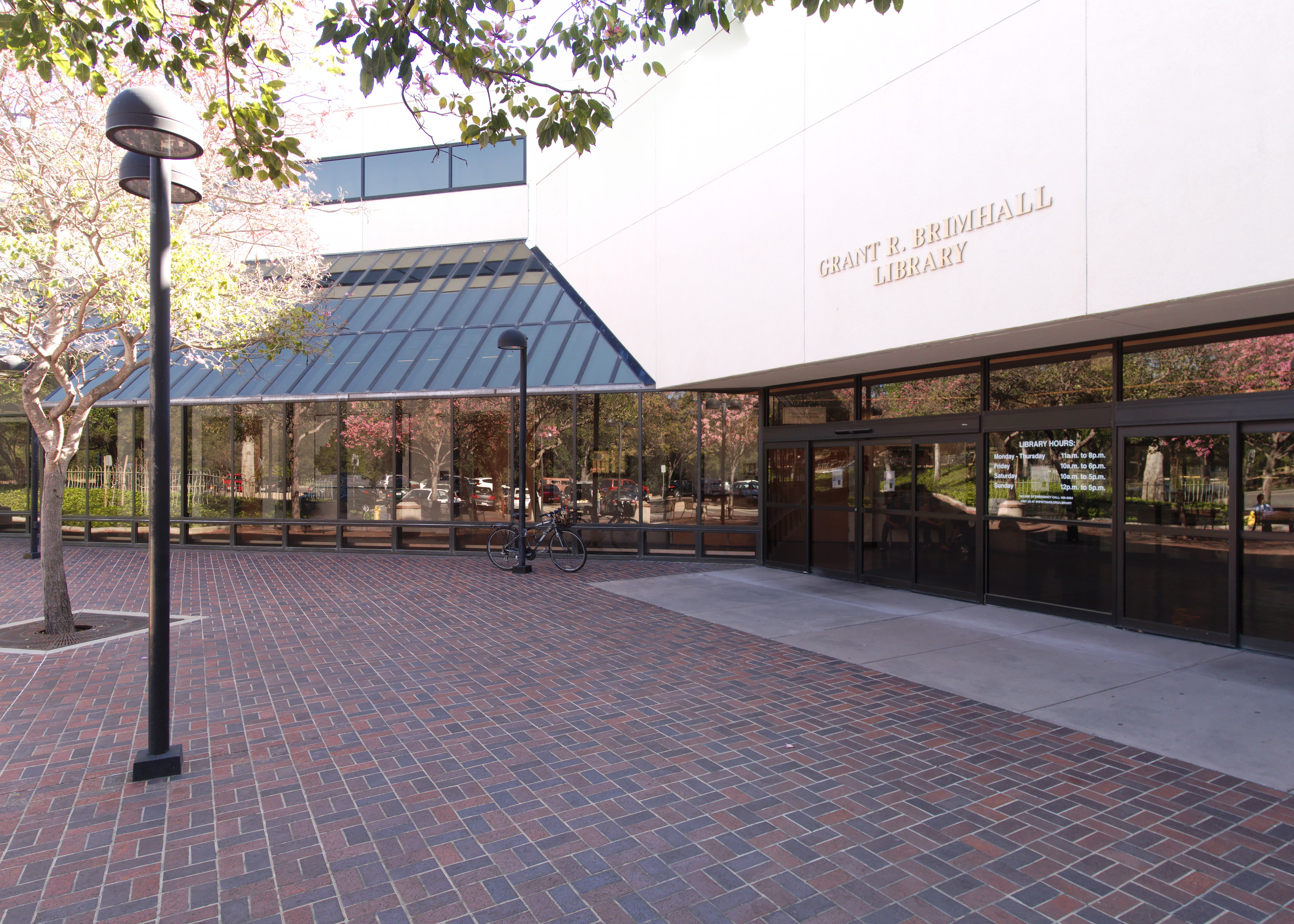 Exterior entrance of a public library with glass doors, a covered walkway, and a brick plaza.