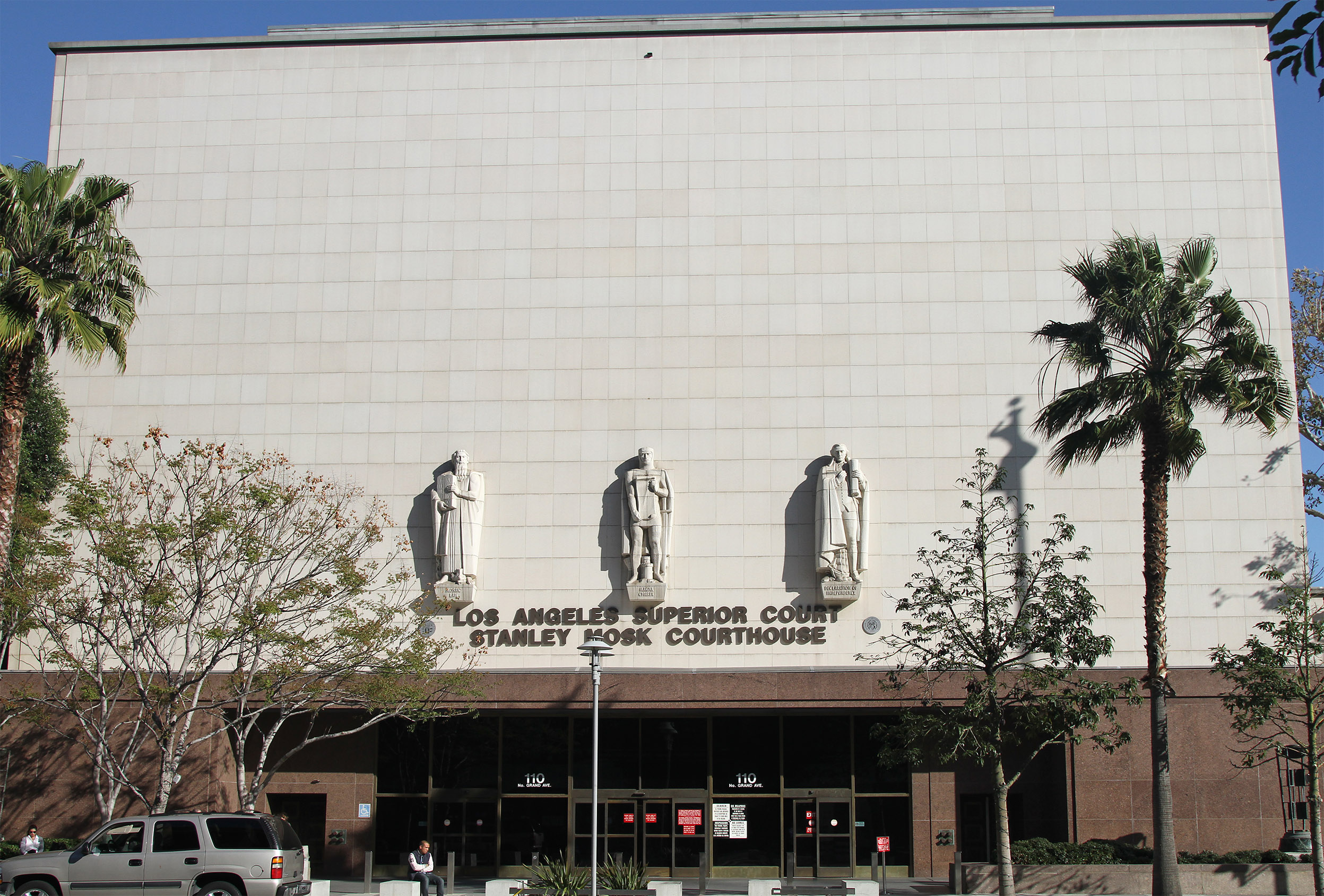 Exterior of a large modernist courthouse with bas-relief statues and palm trees lining the entrance.