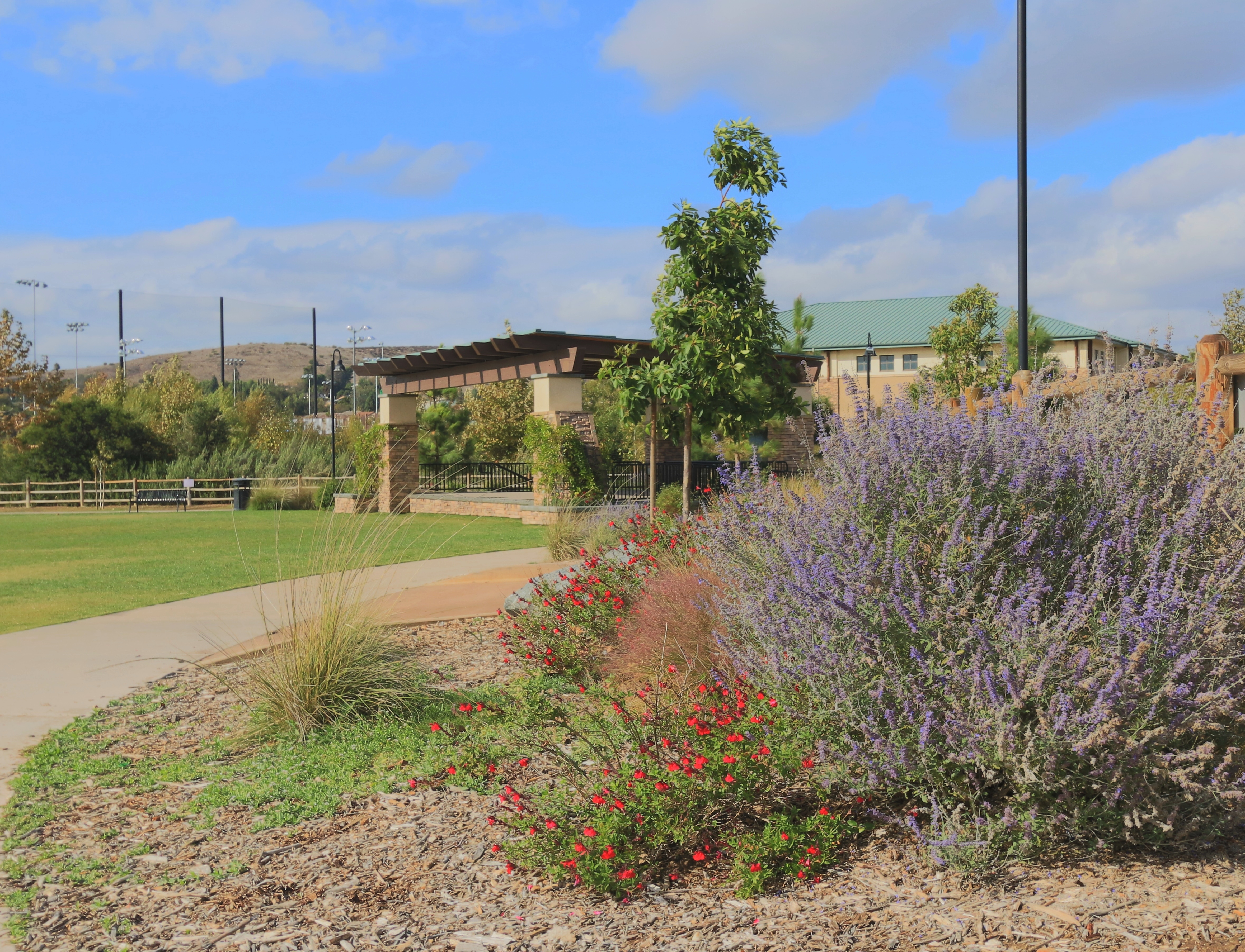 Covered outdoor performance pavilion in a landscaped community park under a partly cloudy sky.