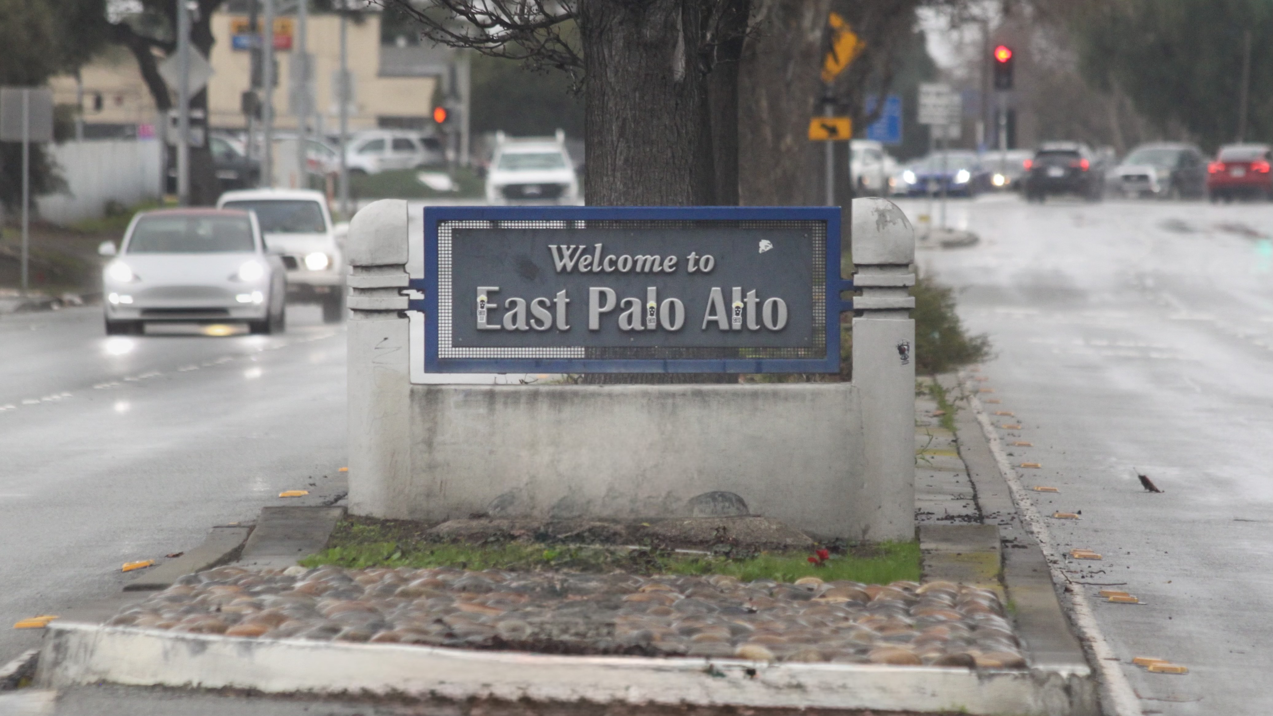 Welcome to East Palo Alto sign on a raised median along a wet street.