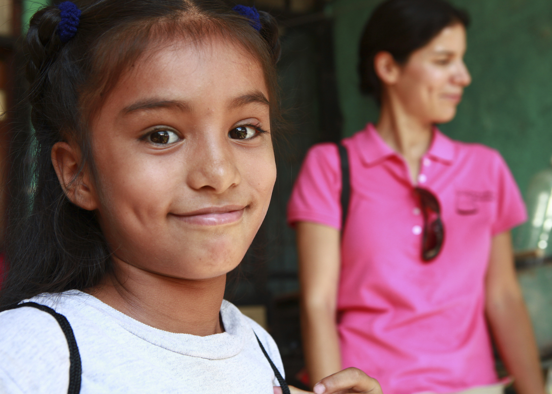 A young girl smiles while wearing a backpack filled with school supplies.