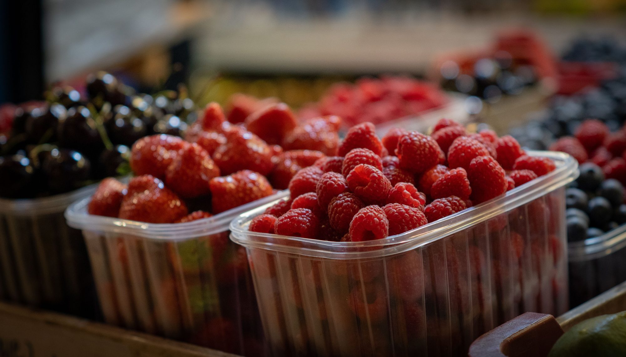 Close-up of fresh raspberries, strawberries, and cherries in plastic containers.