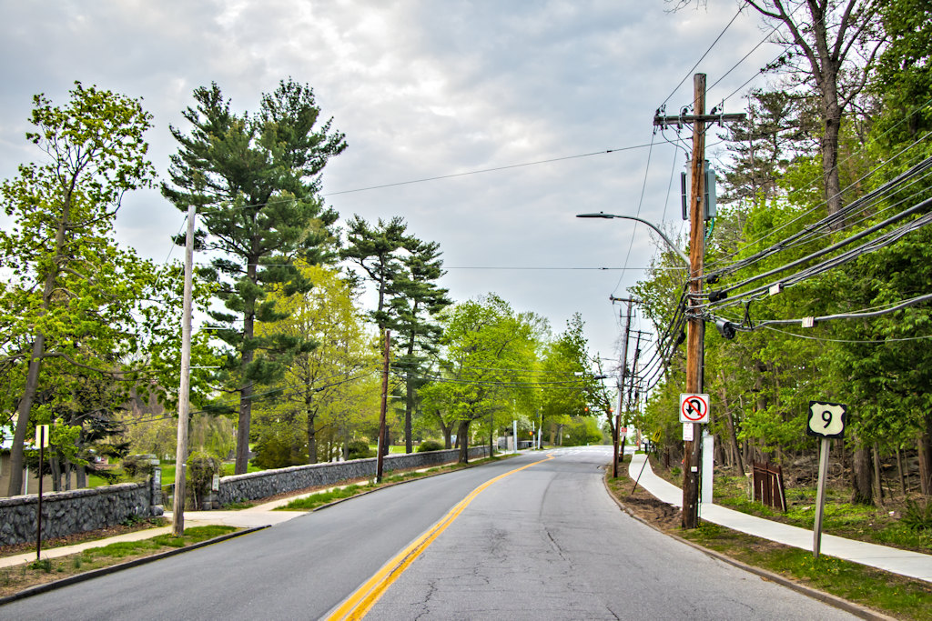 A two-lane road with yellow center line, Route 9 marker sign, utility poles, and stone wall along the side.