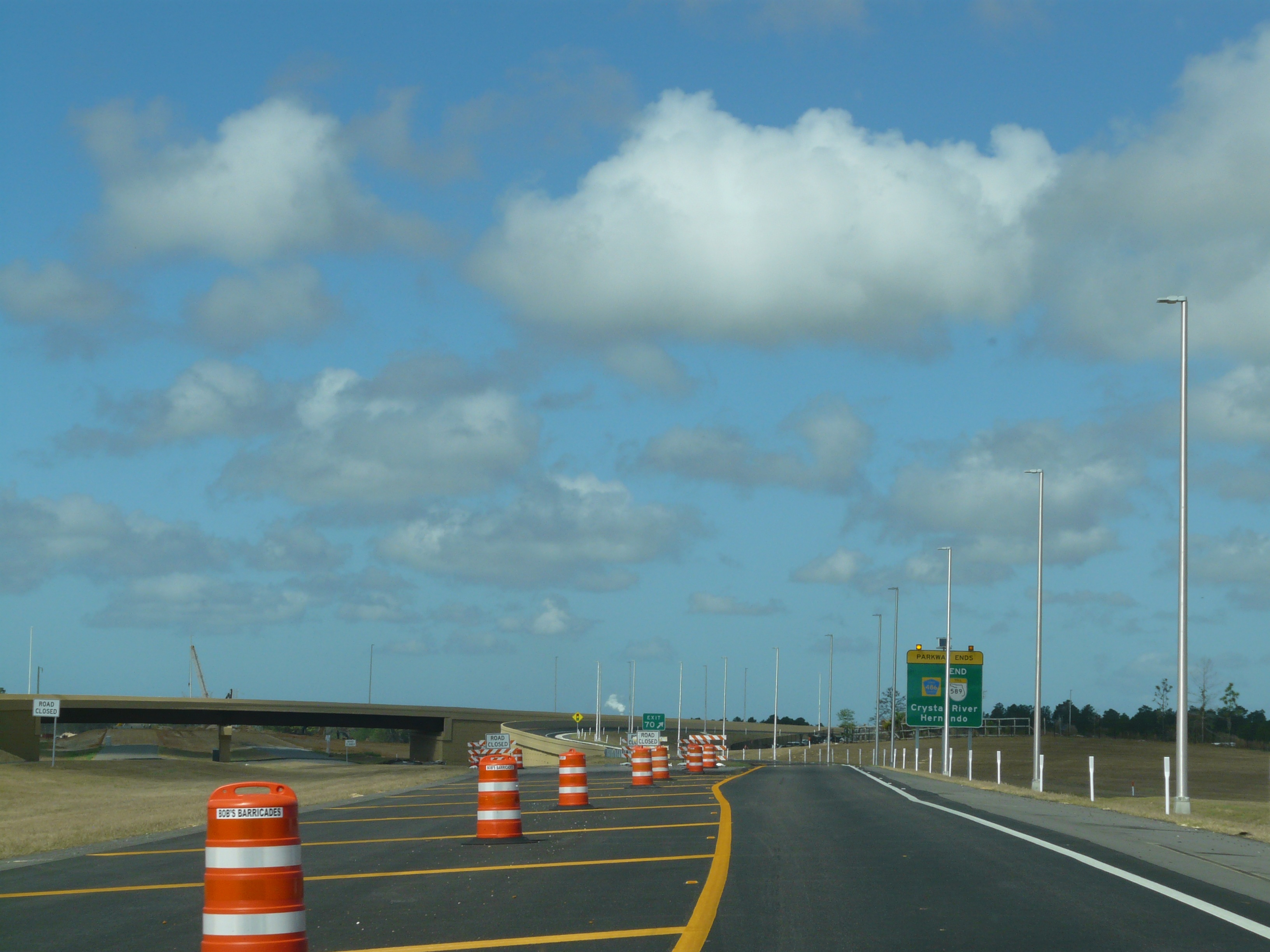 Divided highway lined with orange construction barrels and an overpass bridge ahead.