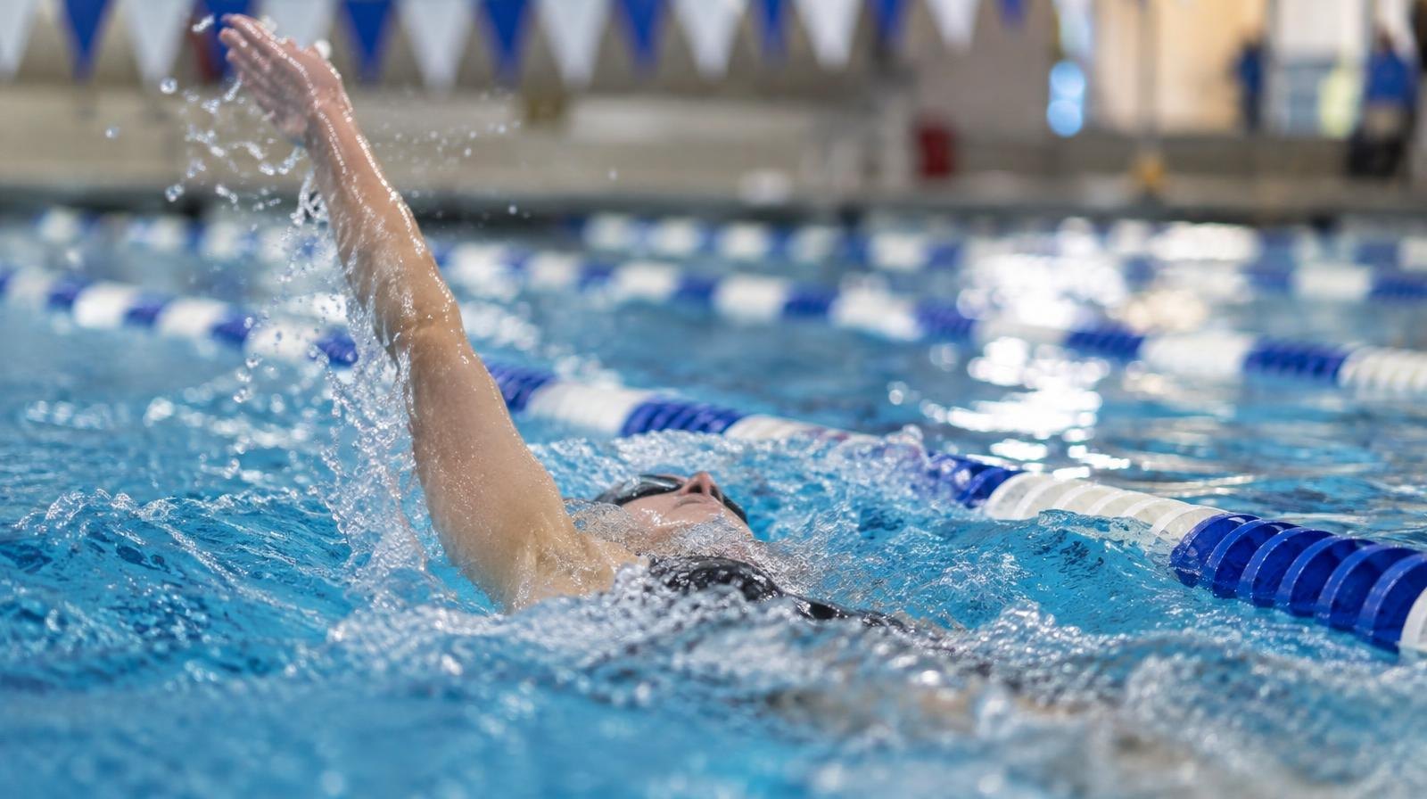 Swimmer performing backstroke in a blue-tiled indoor pool with lane dividers.
