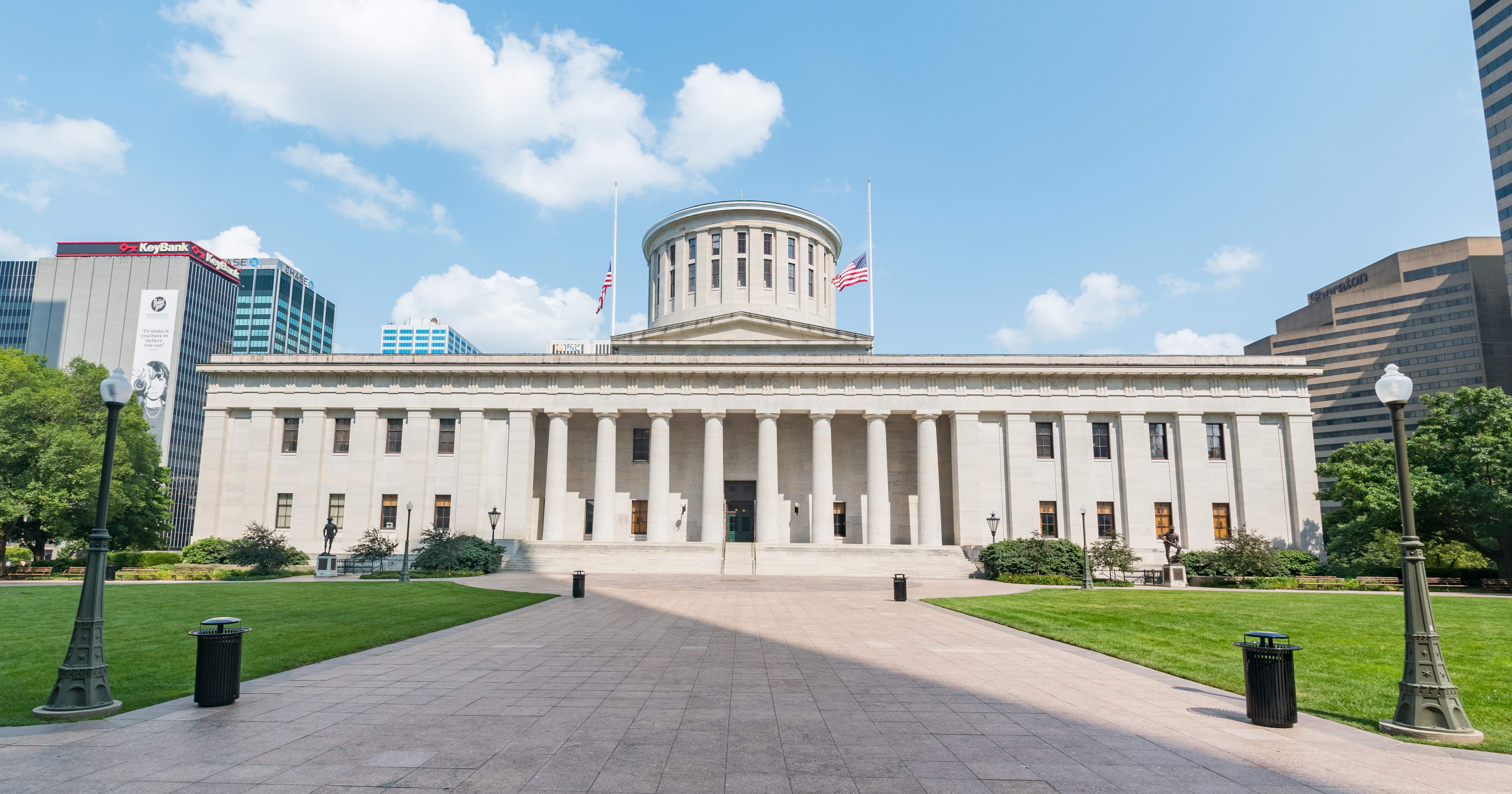 Neoclassical statehouse building with columns, dome, and American flag on a sunny day.