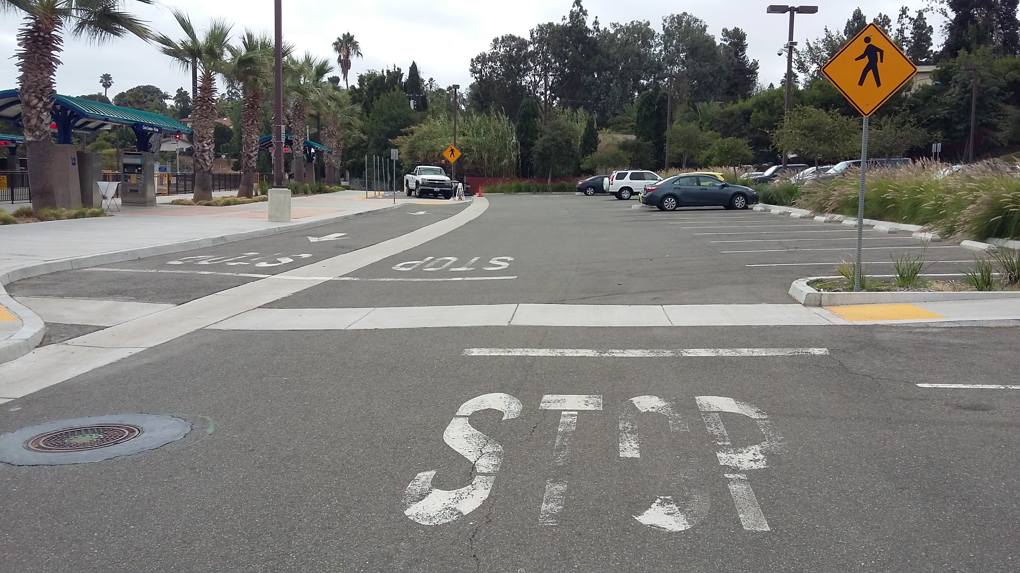 Road surface with STOP markings and a yellow pedestrian crossing warning sign on a pole.