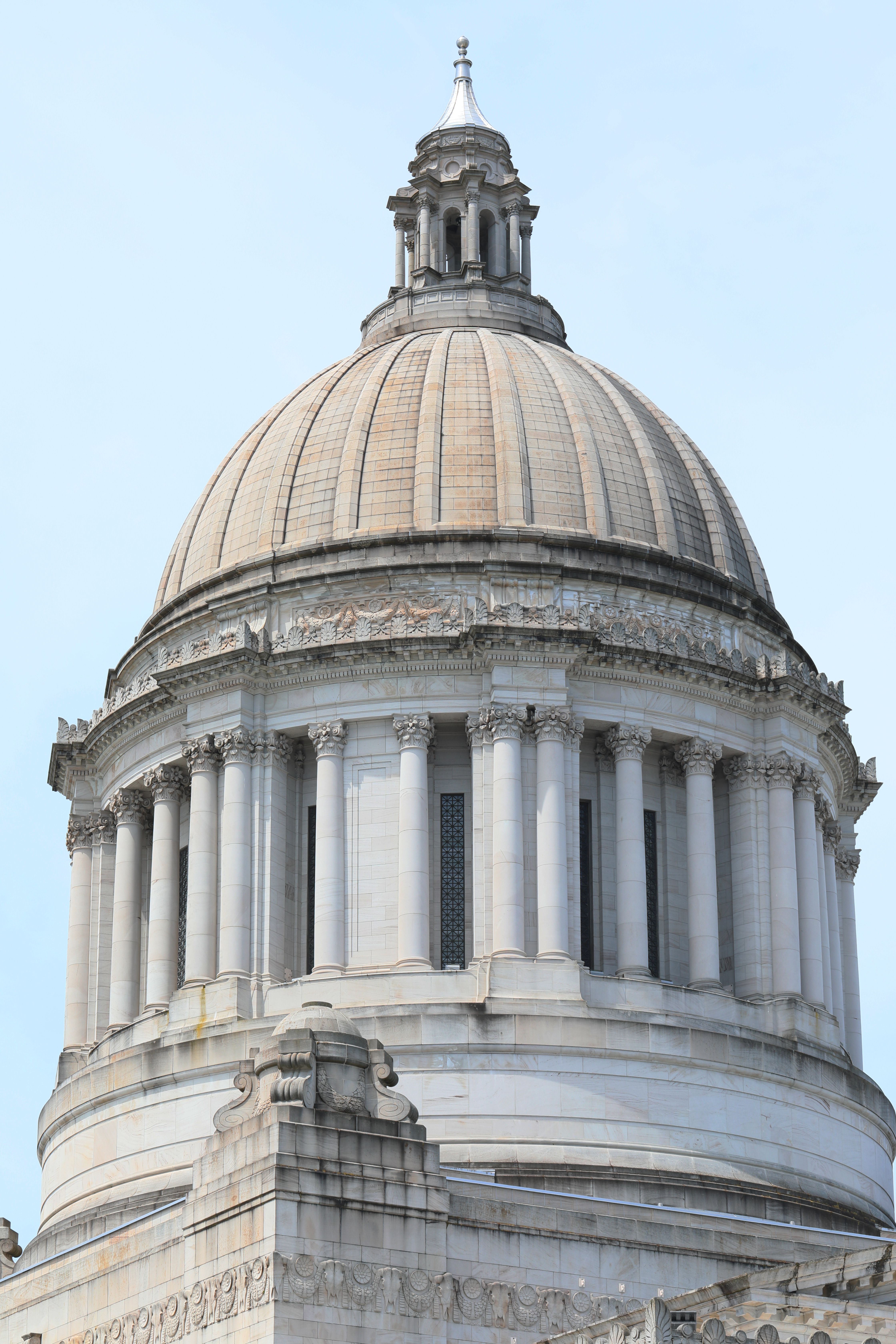 Dome and colonnade of a neoclassical capitol building against a clear blue sky.