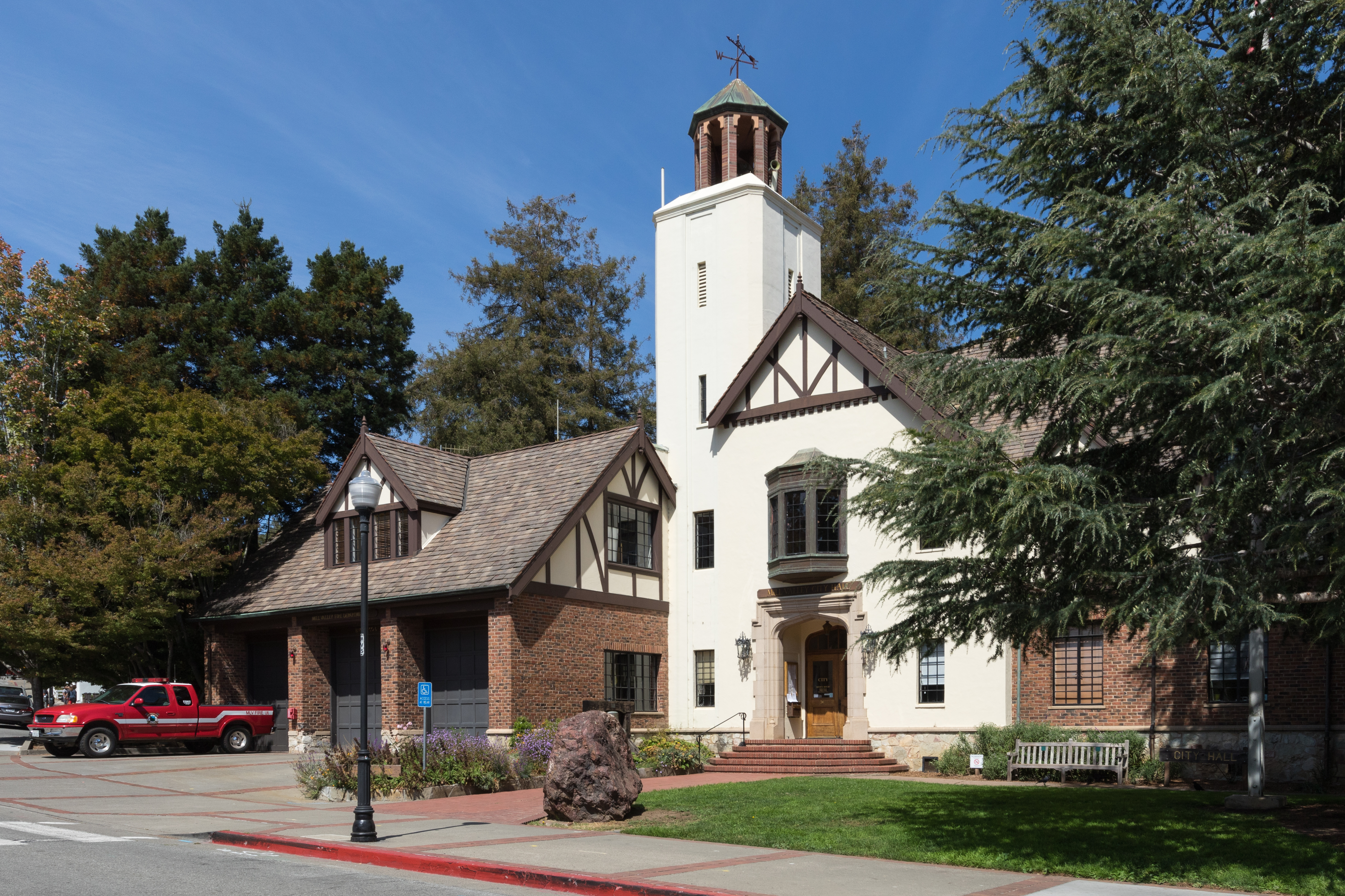 Tudor-style brick and stucco city hall building with white tower and weather vane.