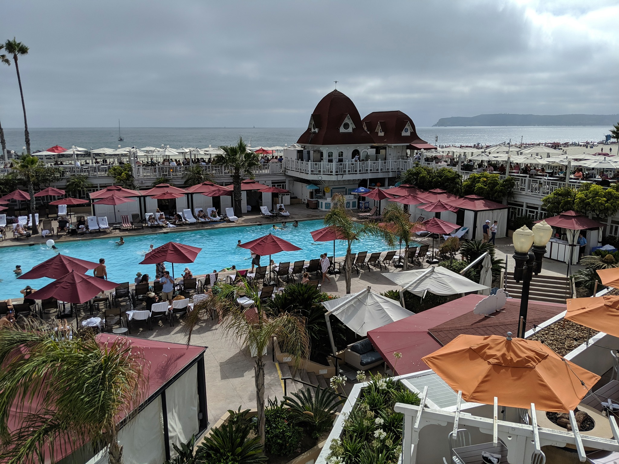 Historic red-roofed Victorian hotel beside an outdoor pool and sandy beach.