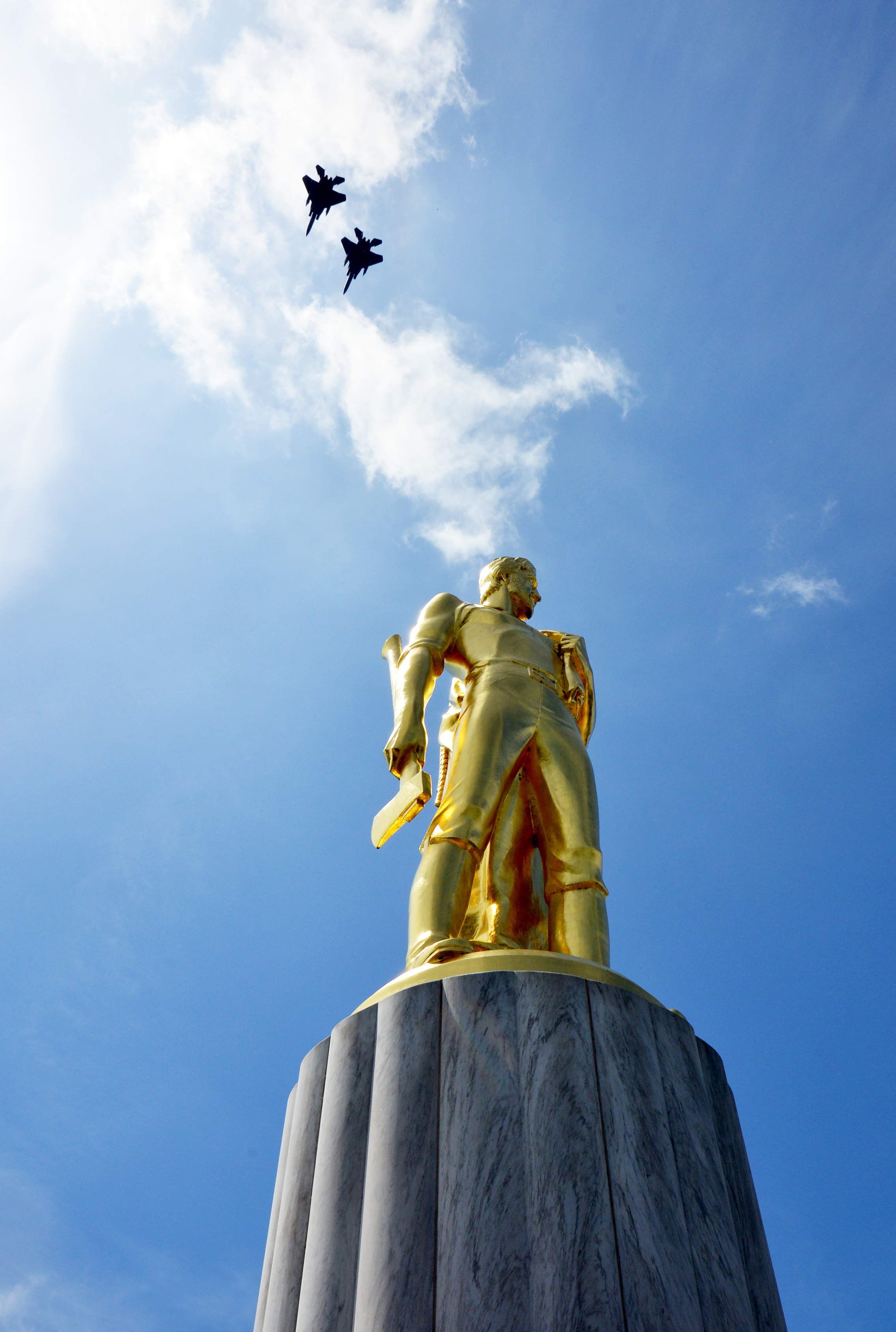 Two military jets fly over the gold-domed Oregon State Capitol against a blue sky.