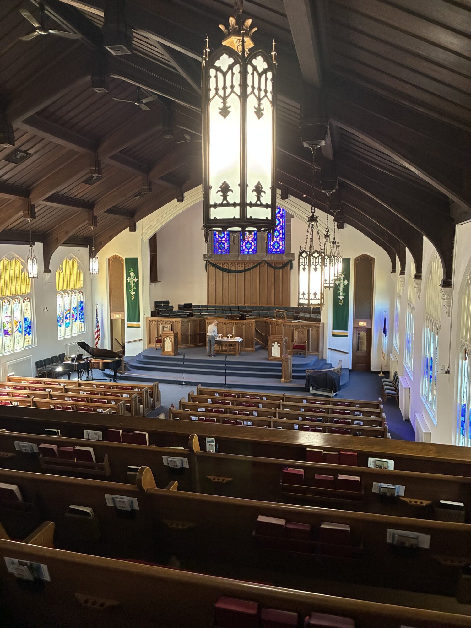 Church sanctuary interior with rows of wooden pews, stained glass windows, and vaulted beamed ceiling.