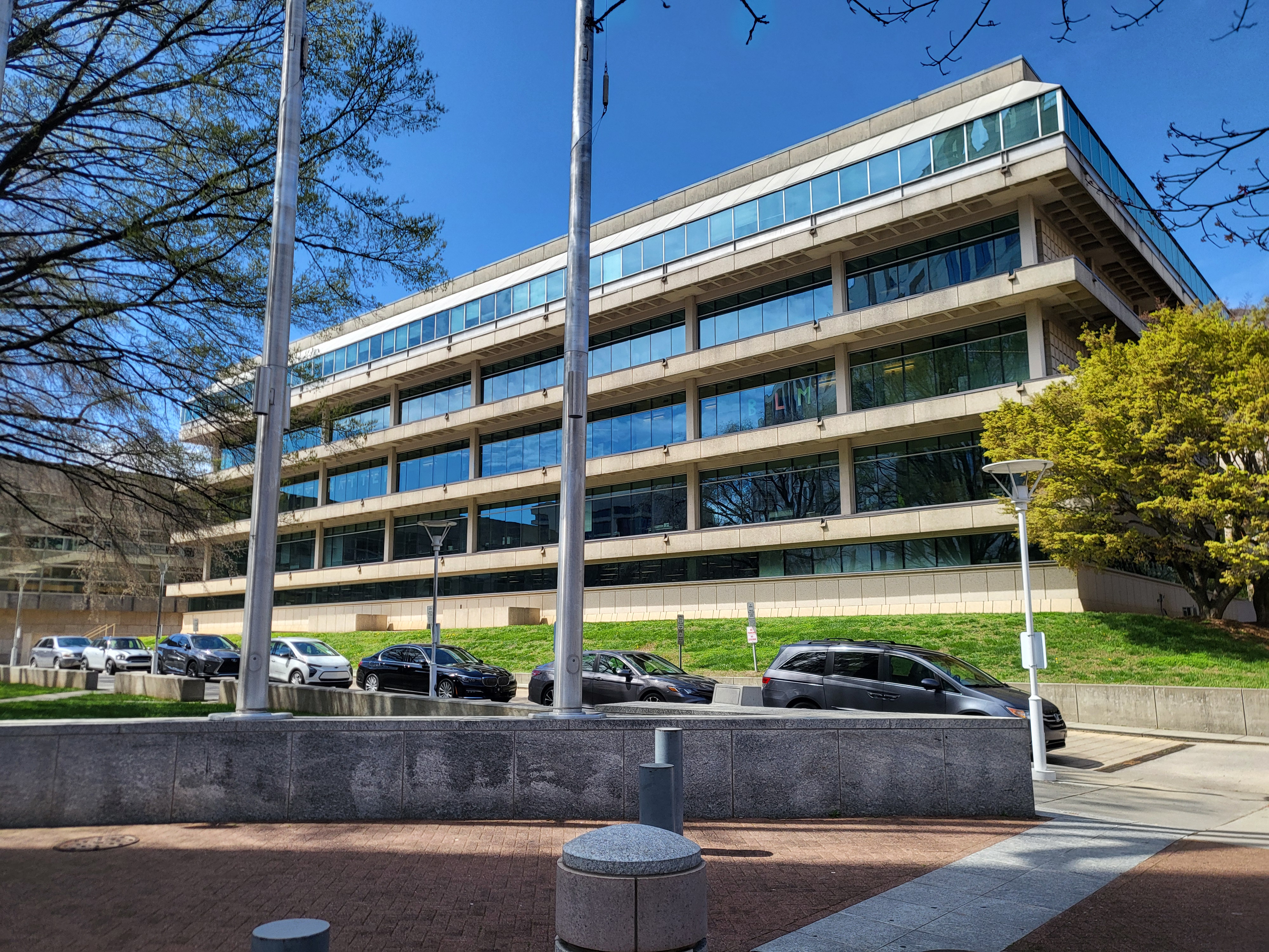 Multi-story government office building with glass facade and flagpoles out front.