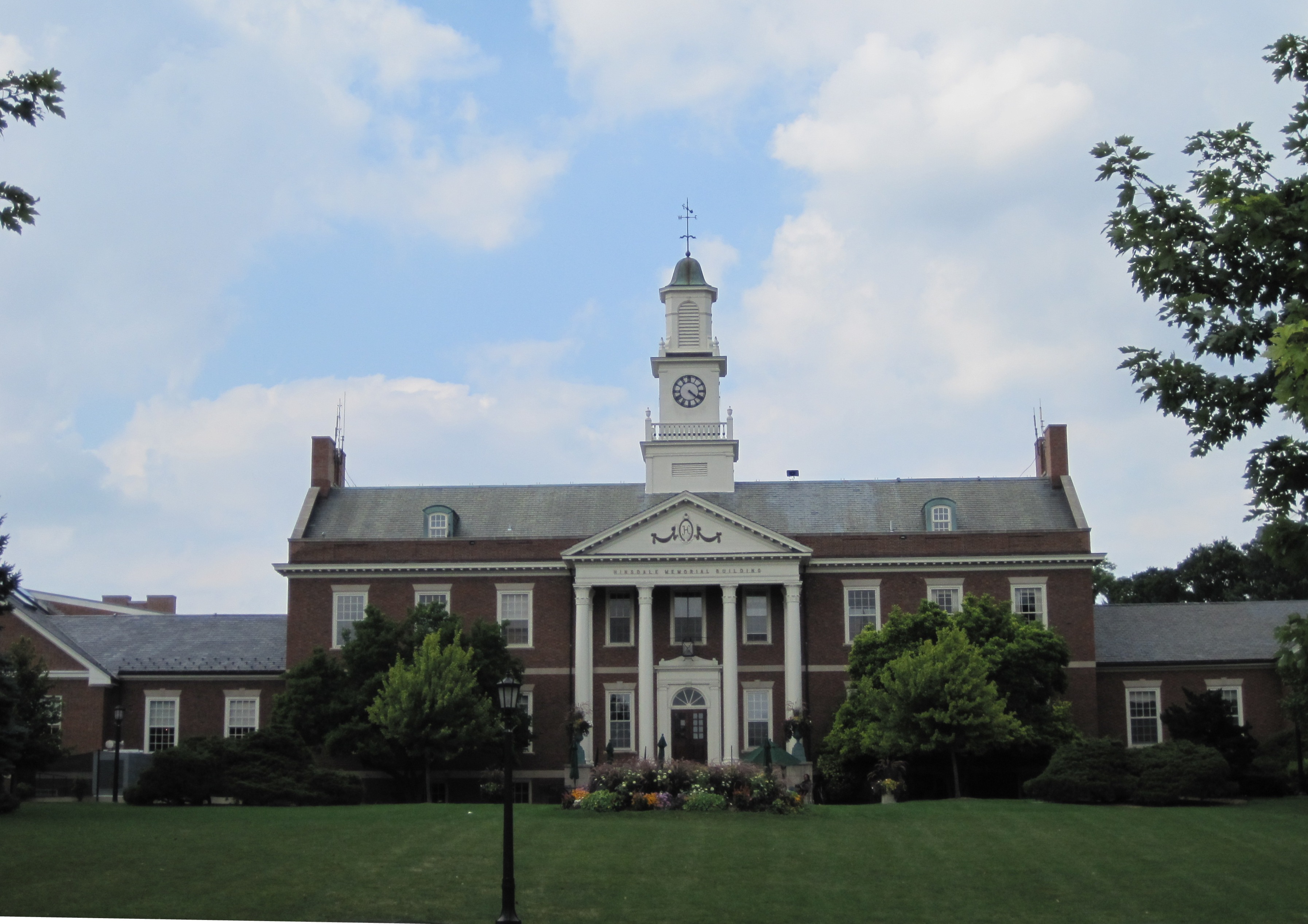 Red brick Colonial Revival building with white clock tower and columned portico on a green lawn.