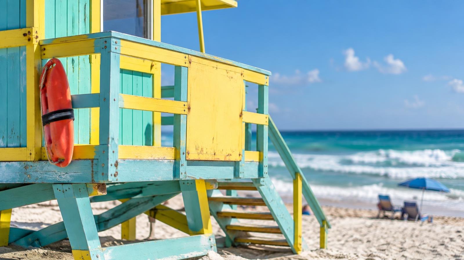 A colorful lifeguard stand on white sand under a clear blue sky.