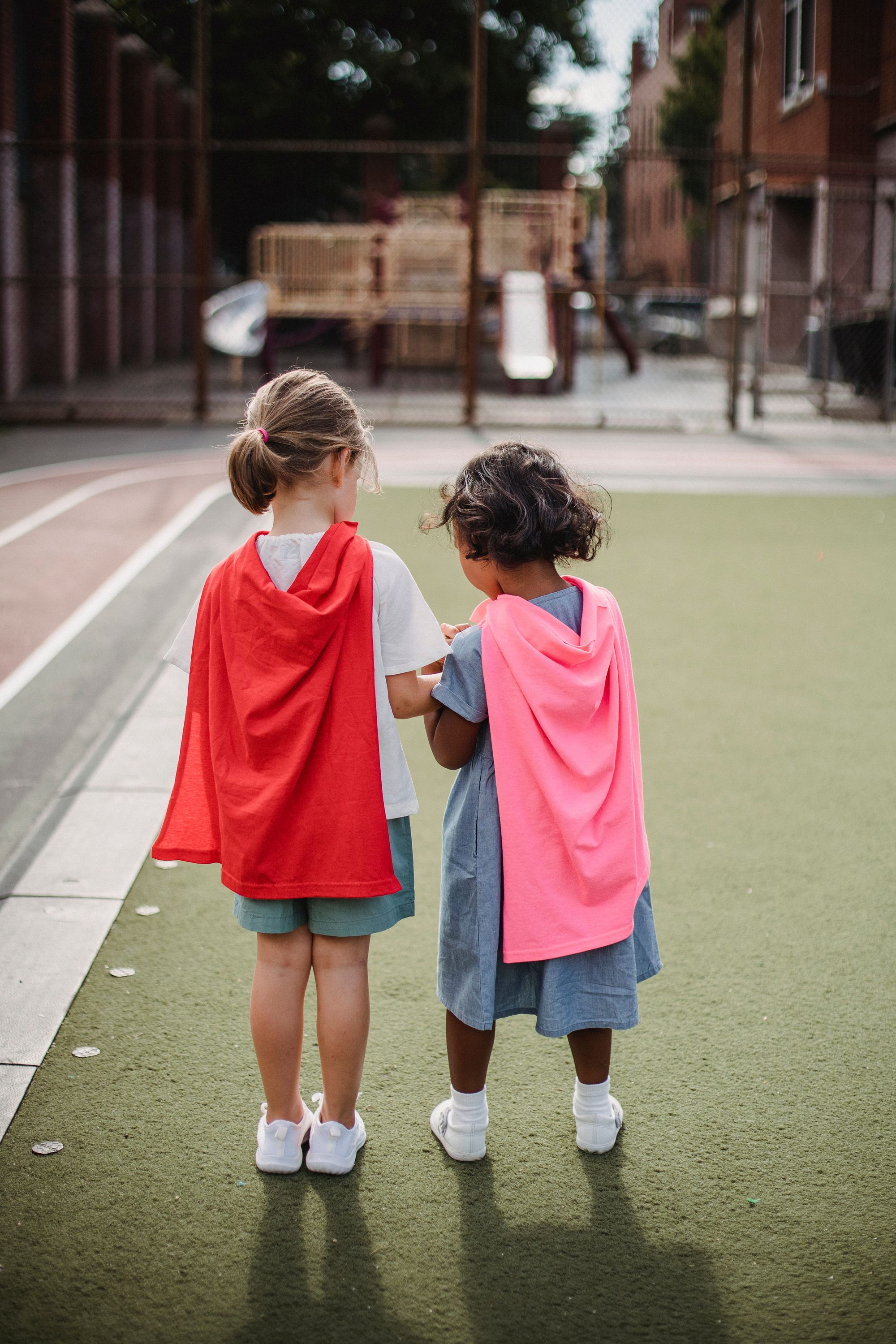 Two girls dressed as superheroes with capes having fun outdoors on a sunny day.