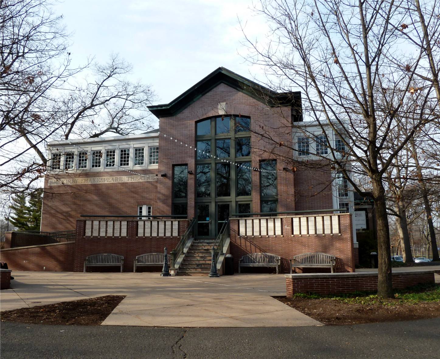 Brick academic building with large glass windows on a college campus, bare trees in foreground.