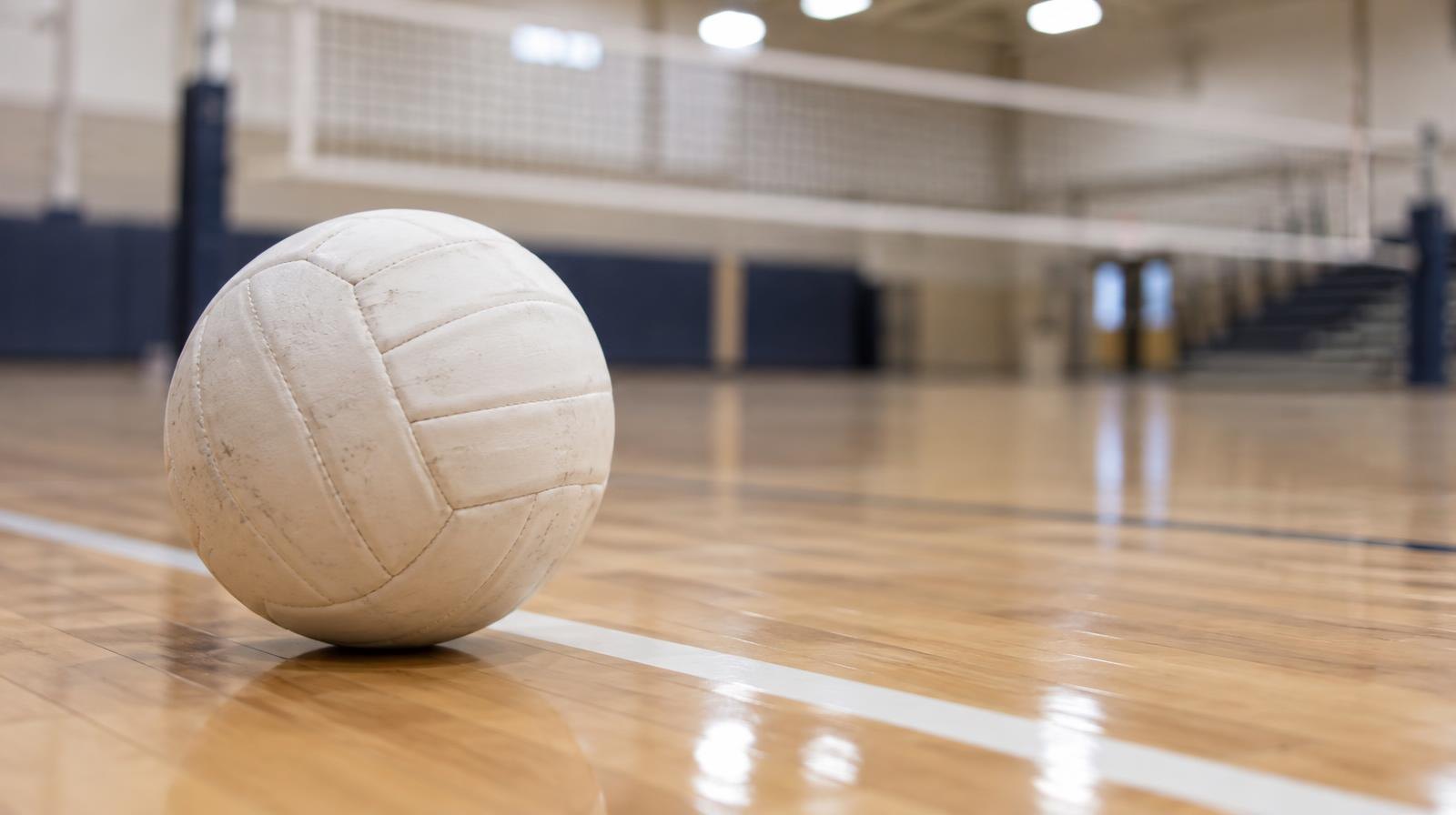 White volleyball resting on a hardwood gym floor near a painted boundary line.