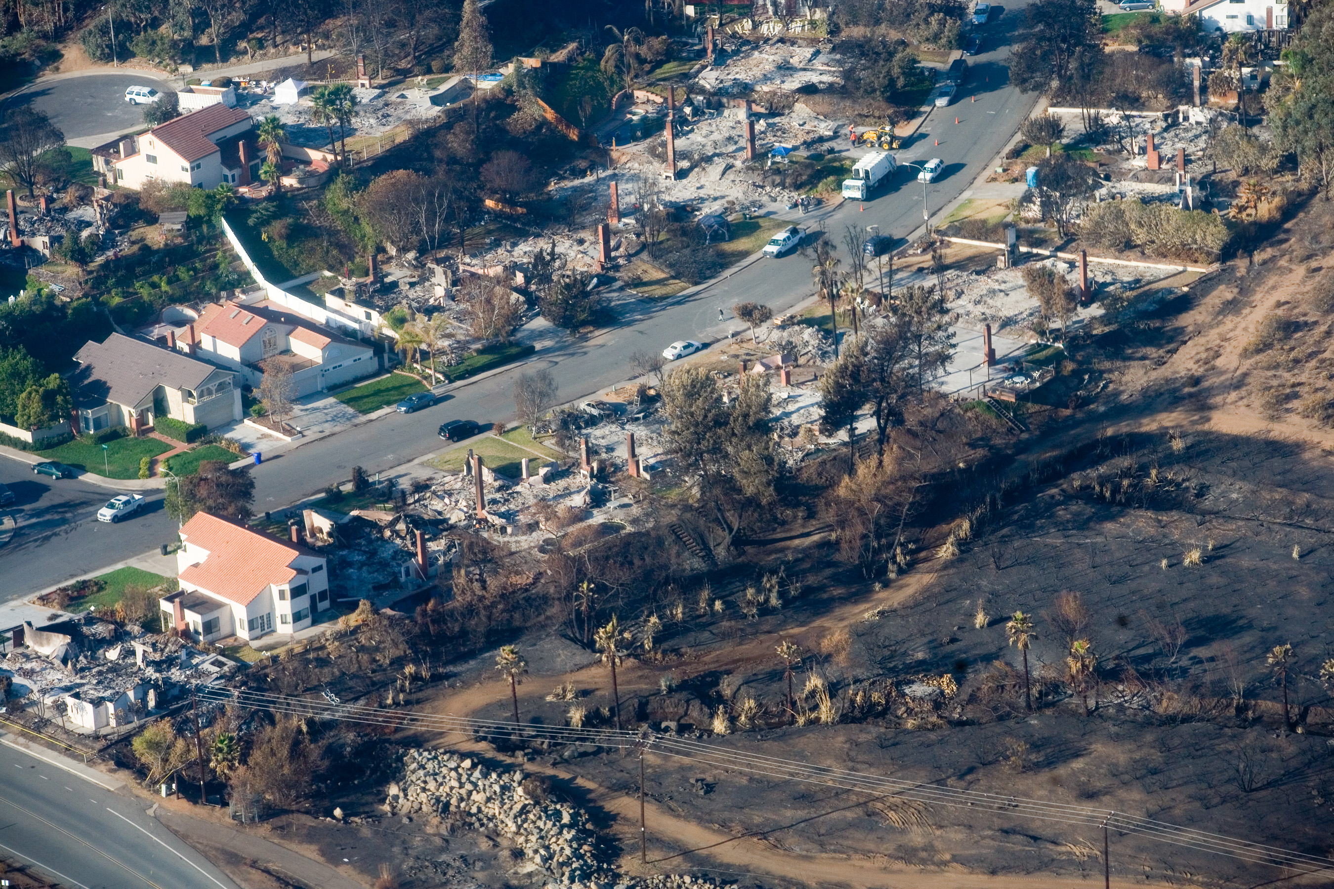 Aerial view of a residential neighborhood with burned foundations and charred debris from wildfire.