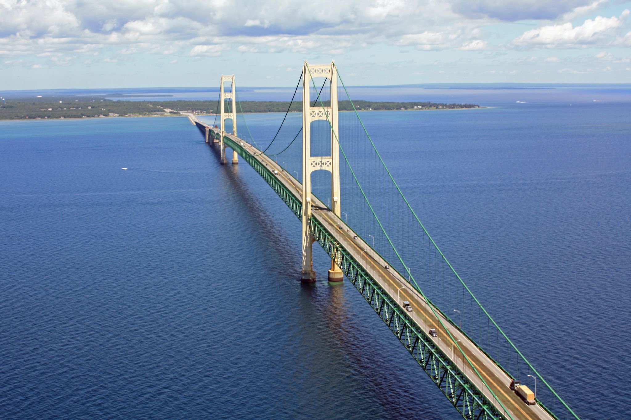 Aerial view of a suspension bridge with green cables spanning blue water and forested shores.
