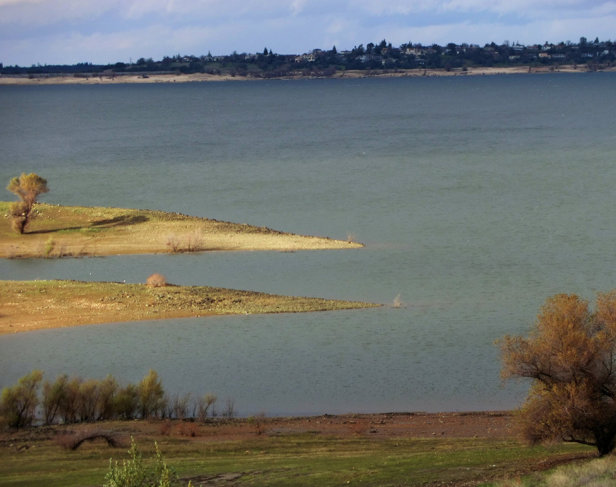 Reservoir with low water levels exposing sandy banks and peninsulas, surrounded by dry hills.