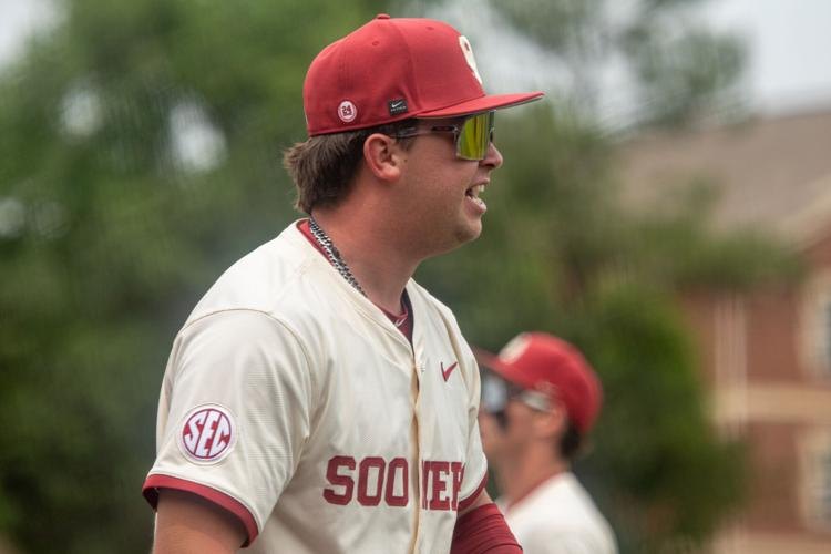 Baseball player in crimson Oklahoma Sooners uniform and yellow-tinted sunglasses on a field.