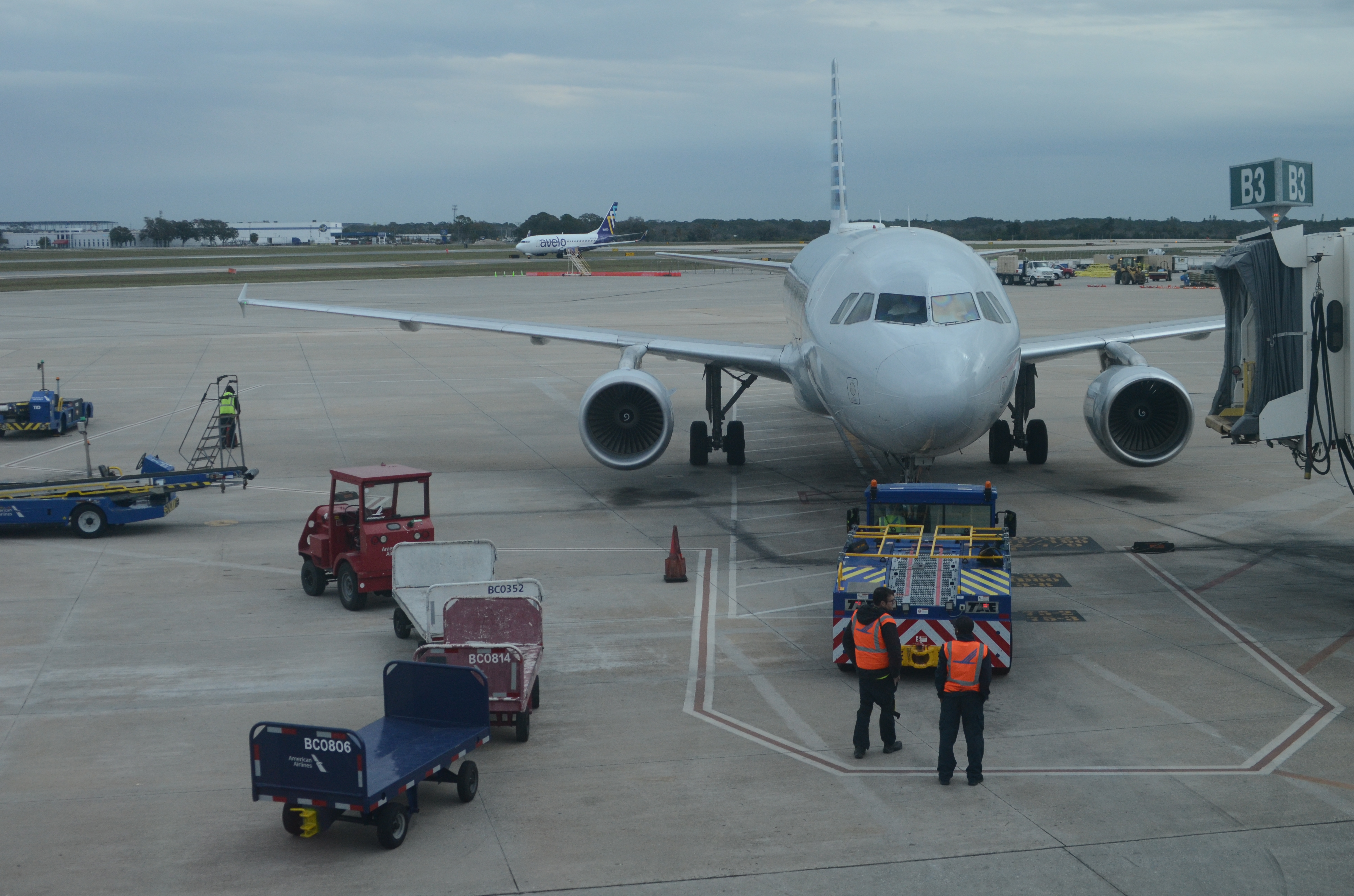 Commercial aircraft parked at the apron of an airport with ground crew nearby.