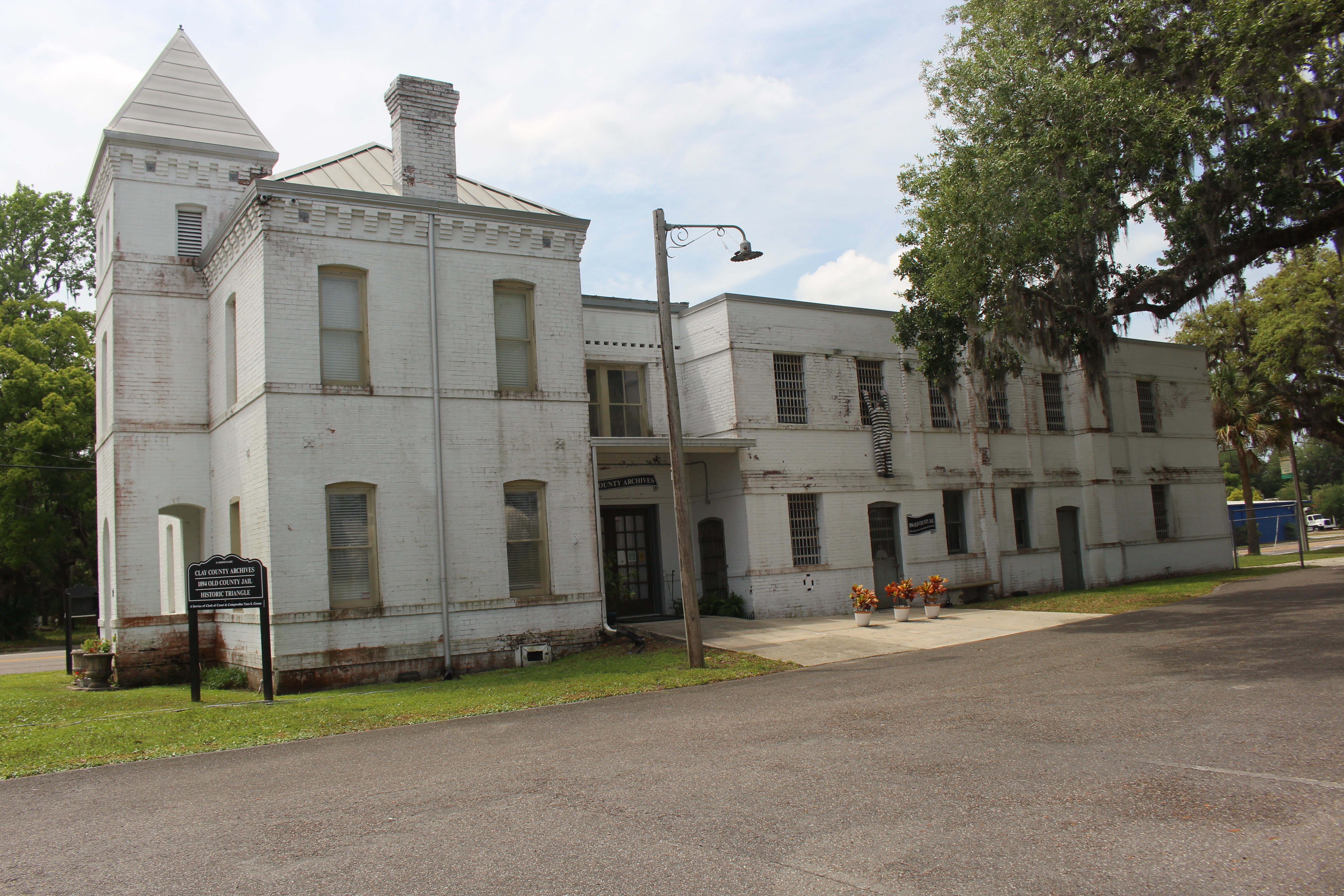 Two-story white historic jail building with pointed turret and street lamp.