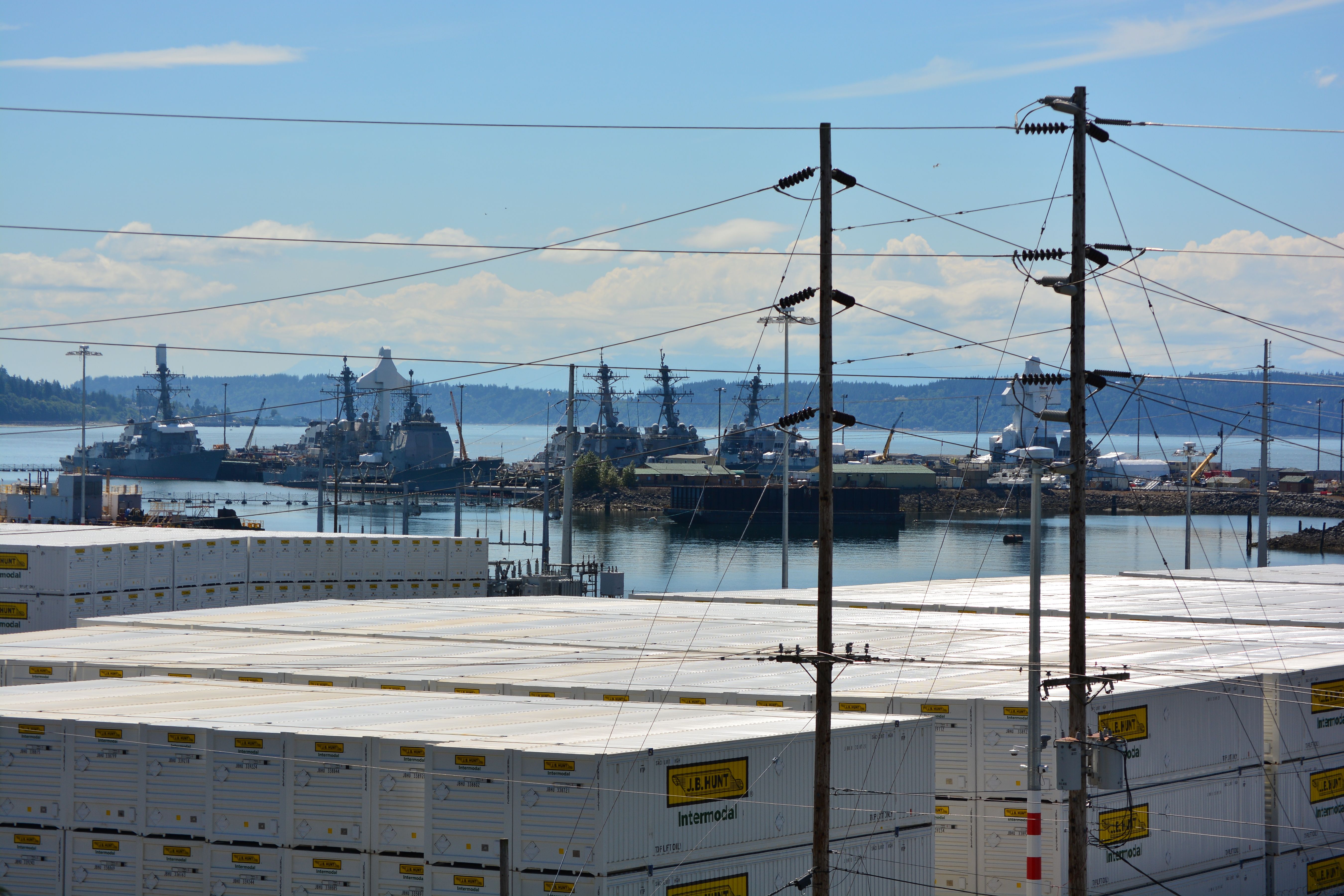 Several Navy ships docked at Naval Station Everett, seen from across the water.